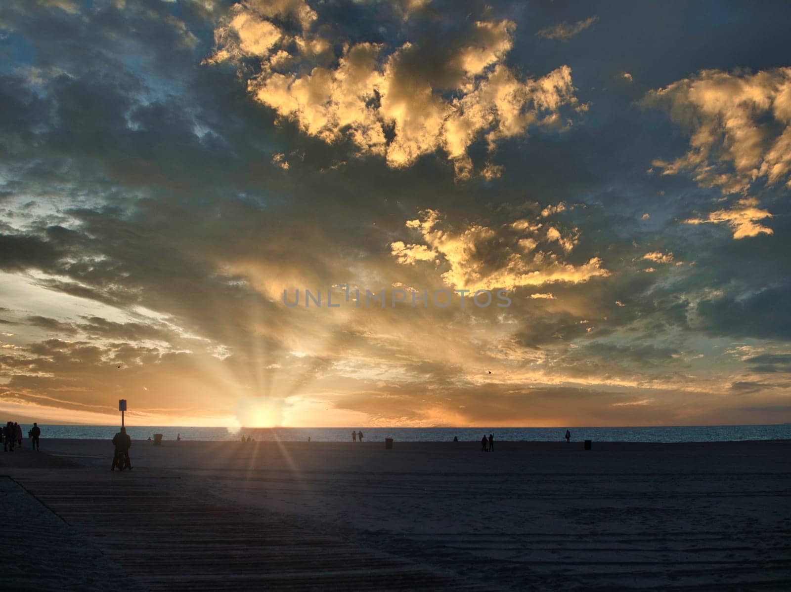 A group of people standing on top of a beach under a cloudy sky. Photo of a group of people enjoying a beach day under a cloudy sky in Los Angeles, California