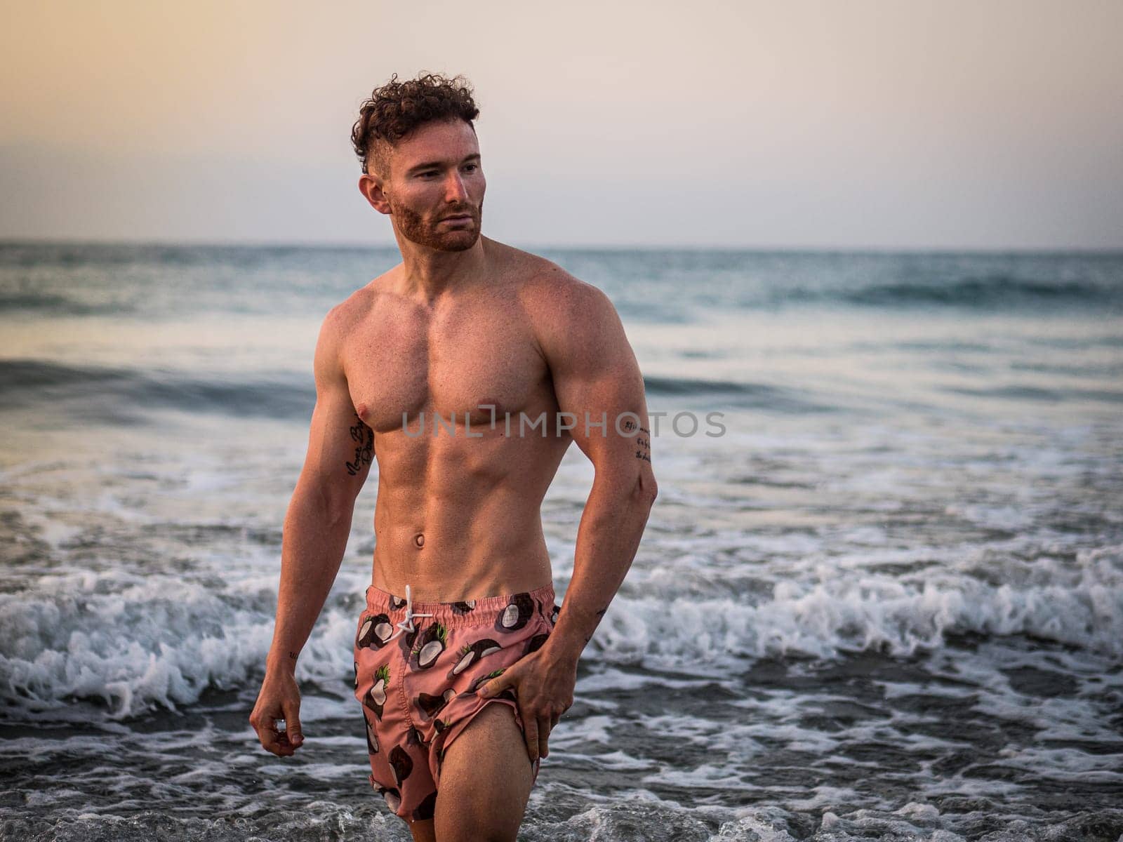A shirtless muscular man walking into the ocean at dawn