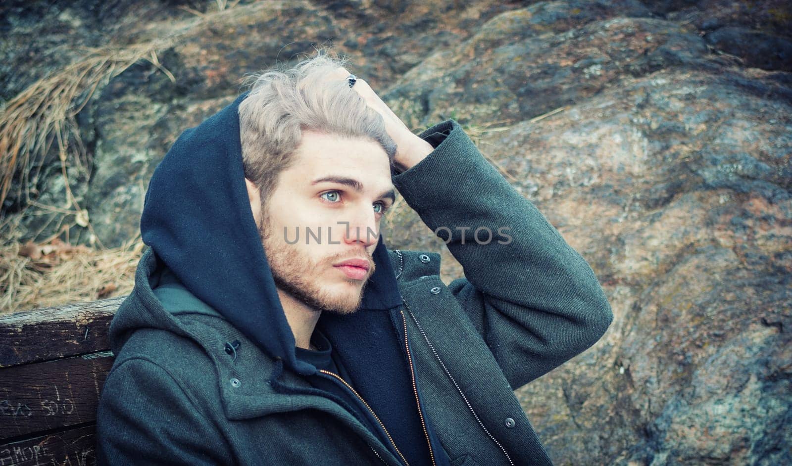 Portrait of young man in hoodie posing outdoor in winter setting with snow all around, looking away to a side.