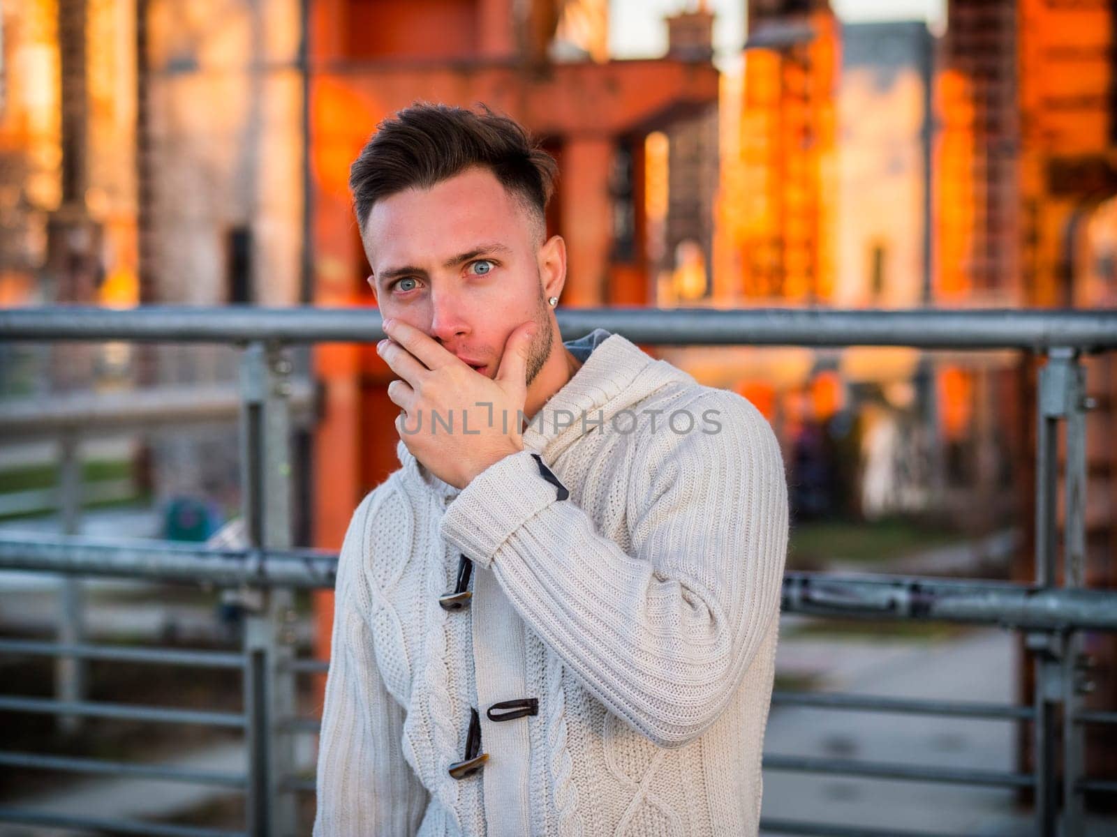 Photo of a man with piercing blue eyes standing in front of a metal fence, with a surprised, scared or worried expression on his face