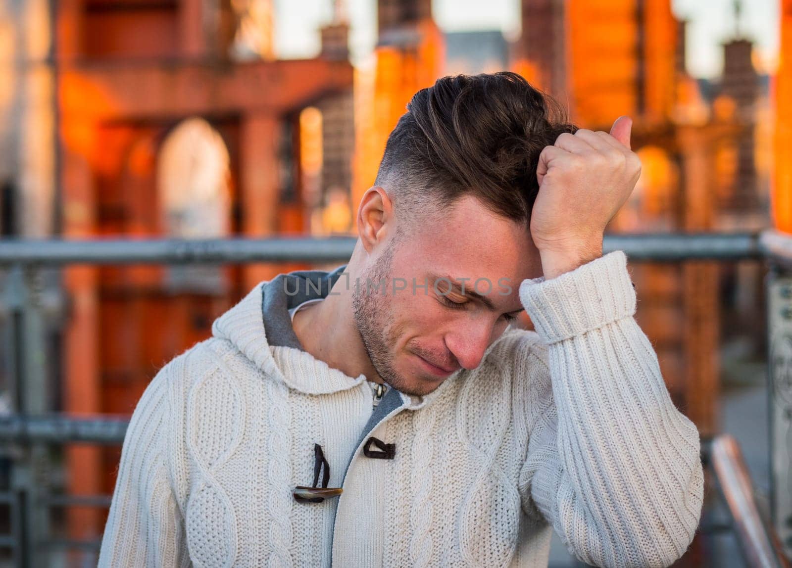 Photo of a man in distress, holding his head in a white sweater