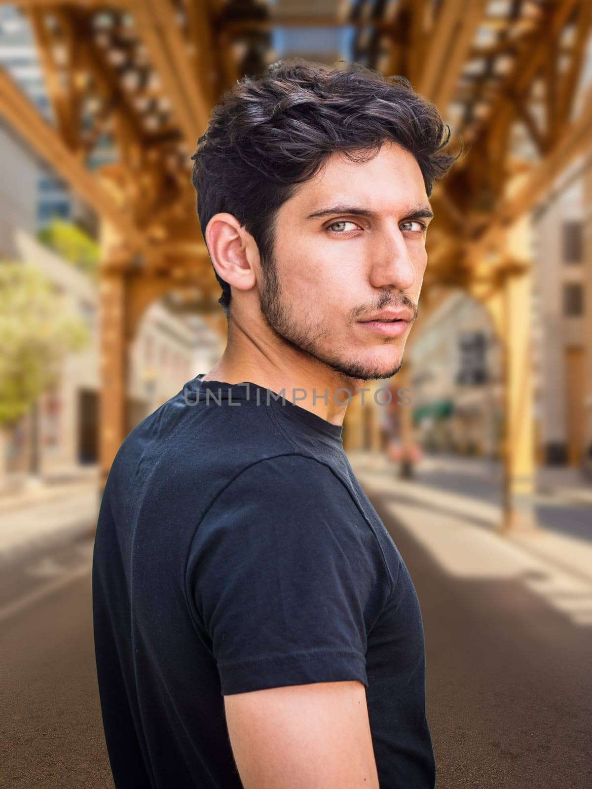 Head and shoulders shot of one handsome young man with green eyes in urban setting, looking at camera, wearing t-shirt