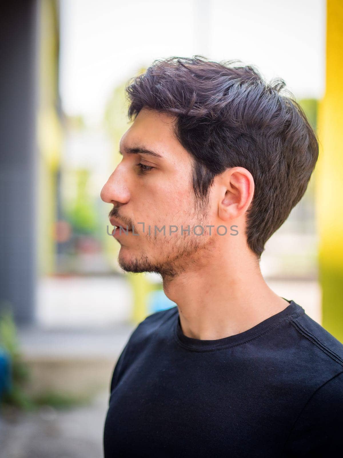 Head and shoulders sideview shot of one handsome young man with green eyes in urban setting, wearing t-shirt