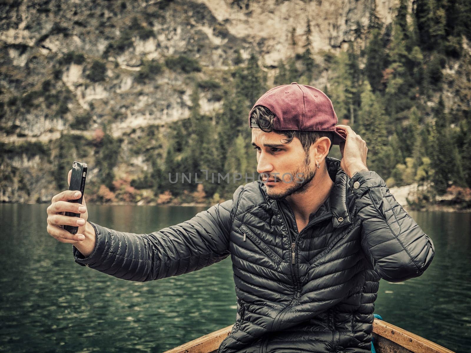 A man sitting in a boat holding a cell phone. Photo of a man enjoying the scenic beauty of the Dolomites in Italy while using his cell phone in a boat