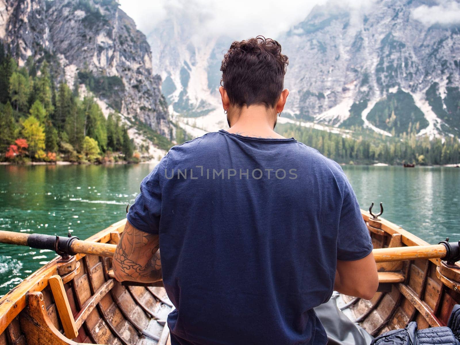 A man sitting in a boat on a lake. Photo of a man peacefully enjoying a boat ride on a serene lake amidst the breathtaking beauty of the Italian Dolomites