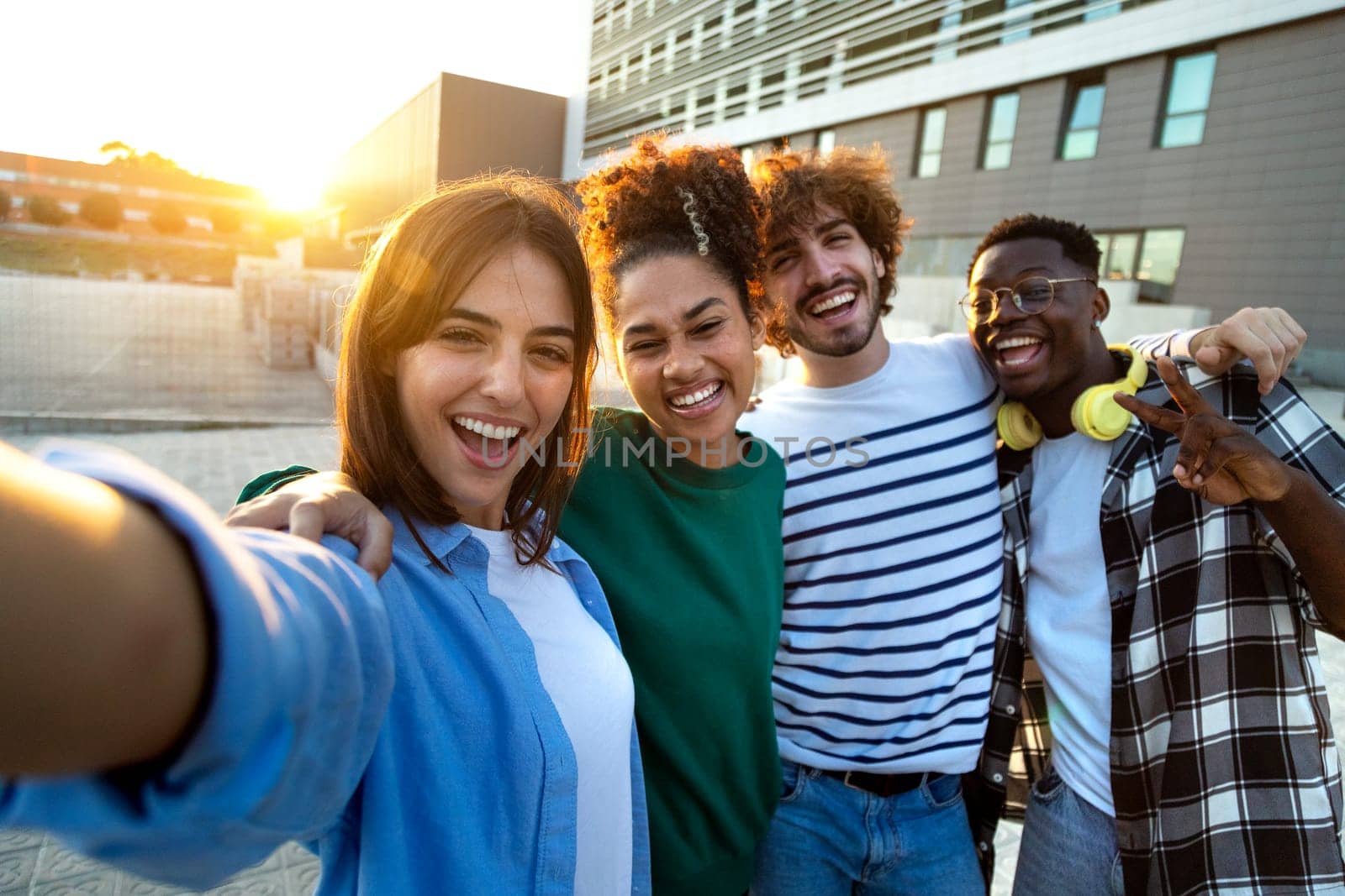 Happy multiracial friends taking selfie and having fun together outdoors in the city during sunset. Looking at camera. by Hoverstock