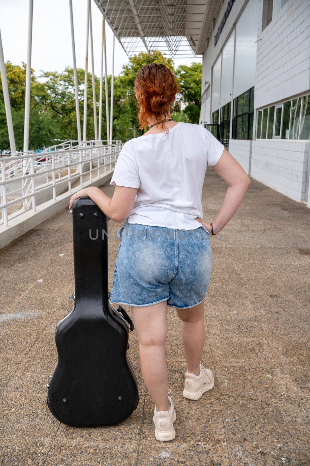young woman with her back leaning glamorously on a guitar case, street music