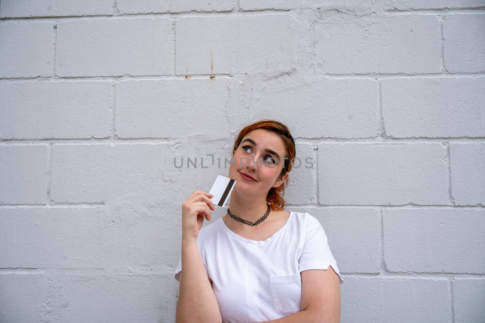 Smiling young woman standing near wall with credit card by barcielaphoto