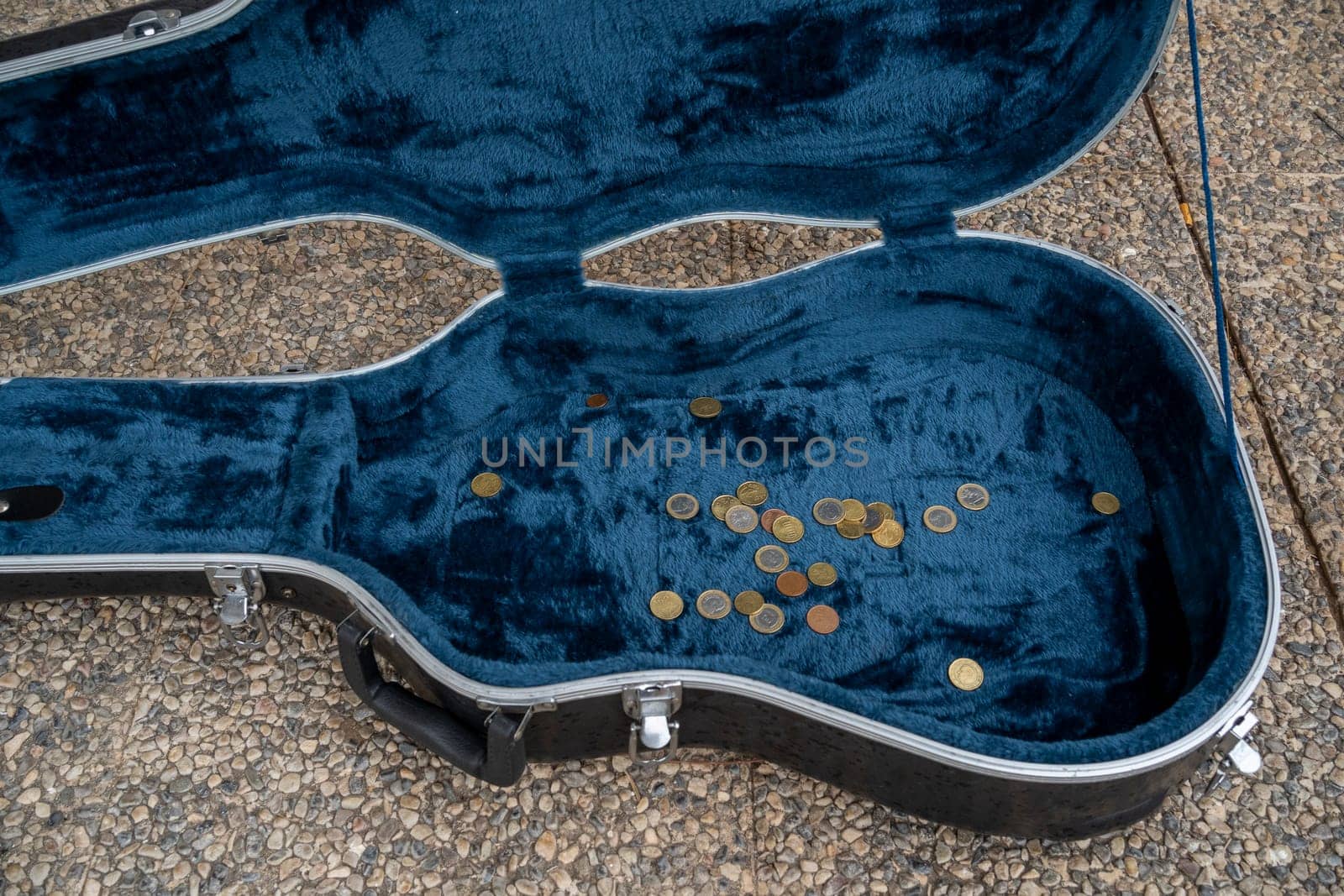 Top view of black opened guitar case with golden coins placed on asphalt pavement during live concert of street performer