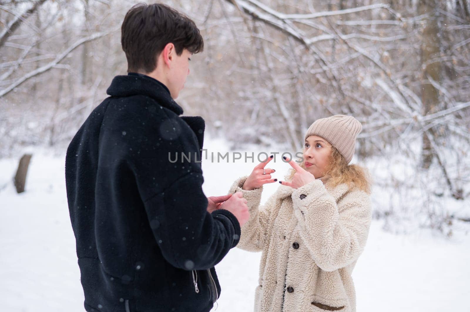 A young couple walks in the winter in the forest. Deaf Guy and a girl communicate using gestures outdoors. by mrwed54