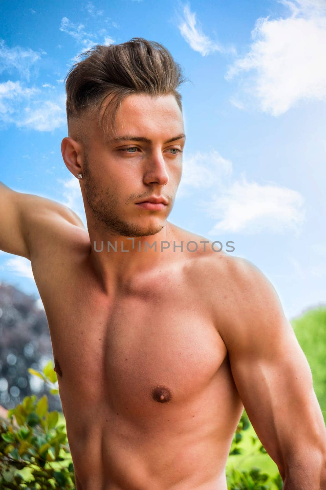 A blond, blue-eyed shirtless young man outdoor against blue sky