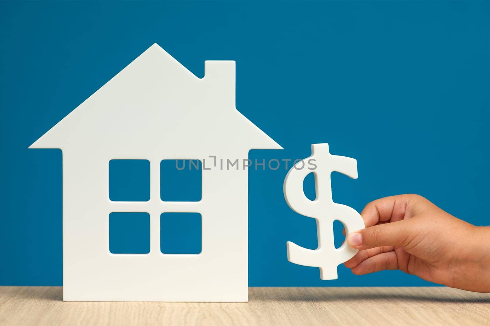 The cost of renting real estate in the USA. Renting residential real estate in America. Model of a white house and a hand with a dollar symbol on a blue background close-up. copy space by SERSOL