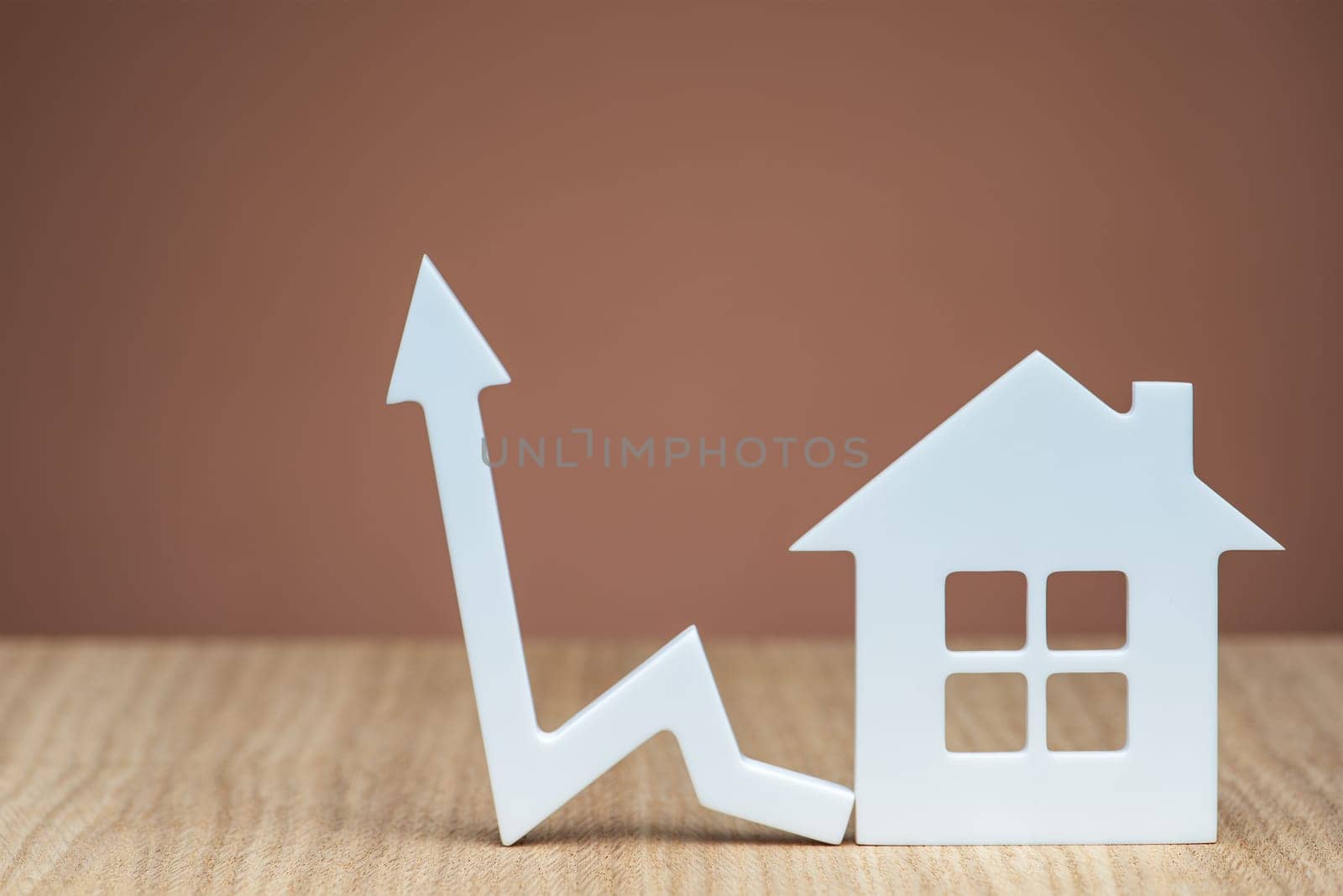 An increase in the interest rate for a mortgage or an increase in the cost of insurance for a property. White house model and graphic arrow pointing up close up on brown background. copy space