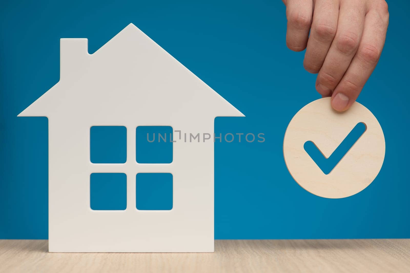 Real estate mortgage approval. Check mark icon in hand and house model as a symbol of a successful real estate purchase or sale deal. Photo with blue background and copy space