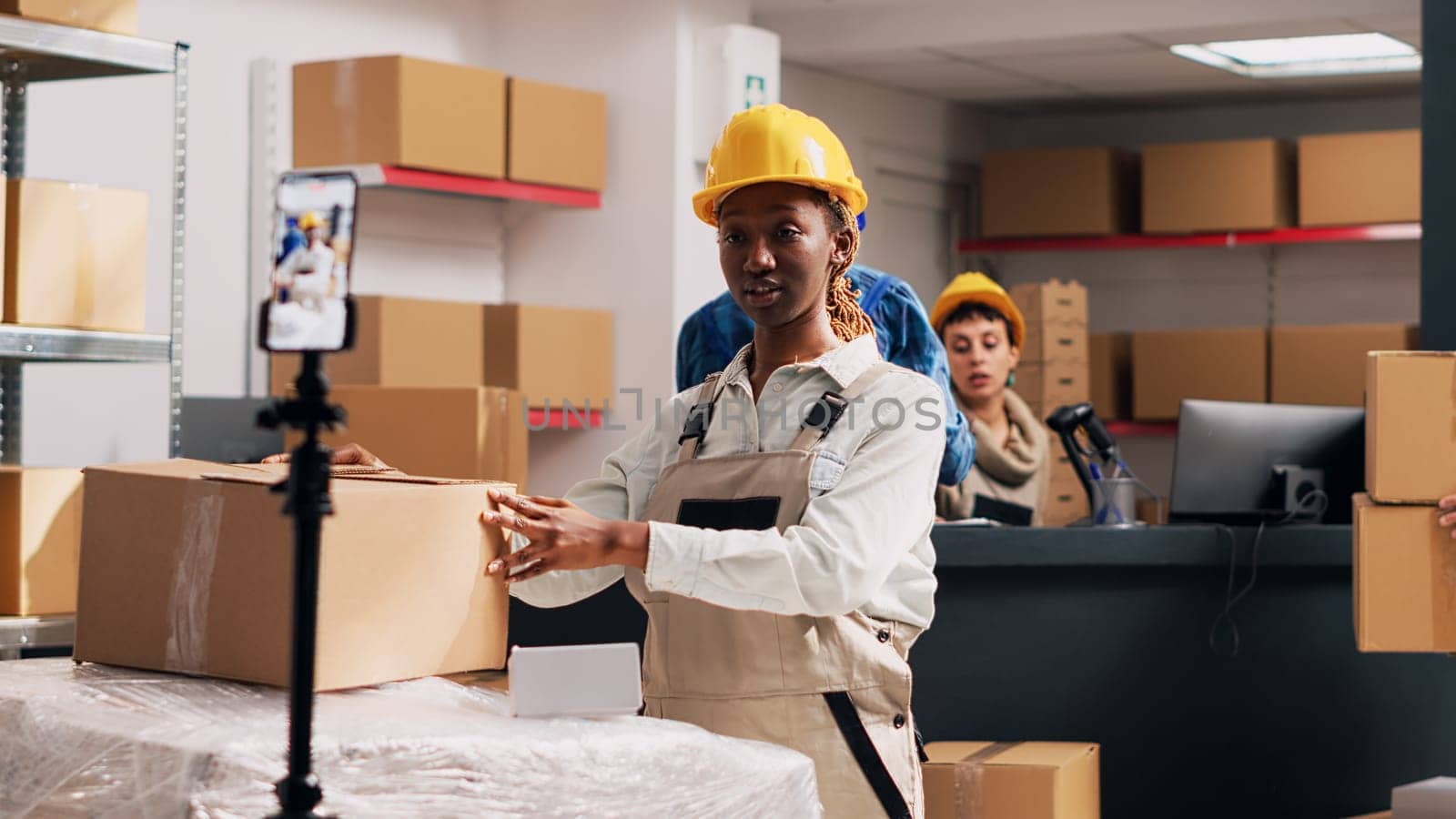 African american girl in overalls filming PR video for social media, creating advertisement for warehouse storage in boxes. Woman recording video on smartphone, stock merchandise. Handheld shot.