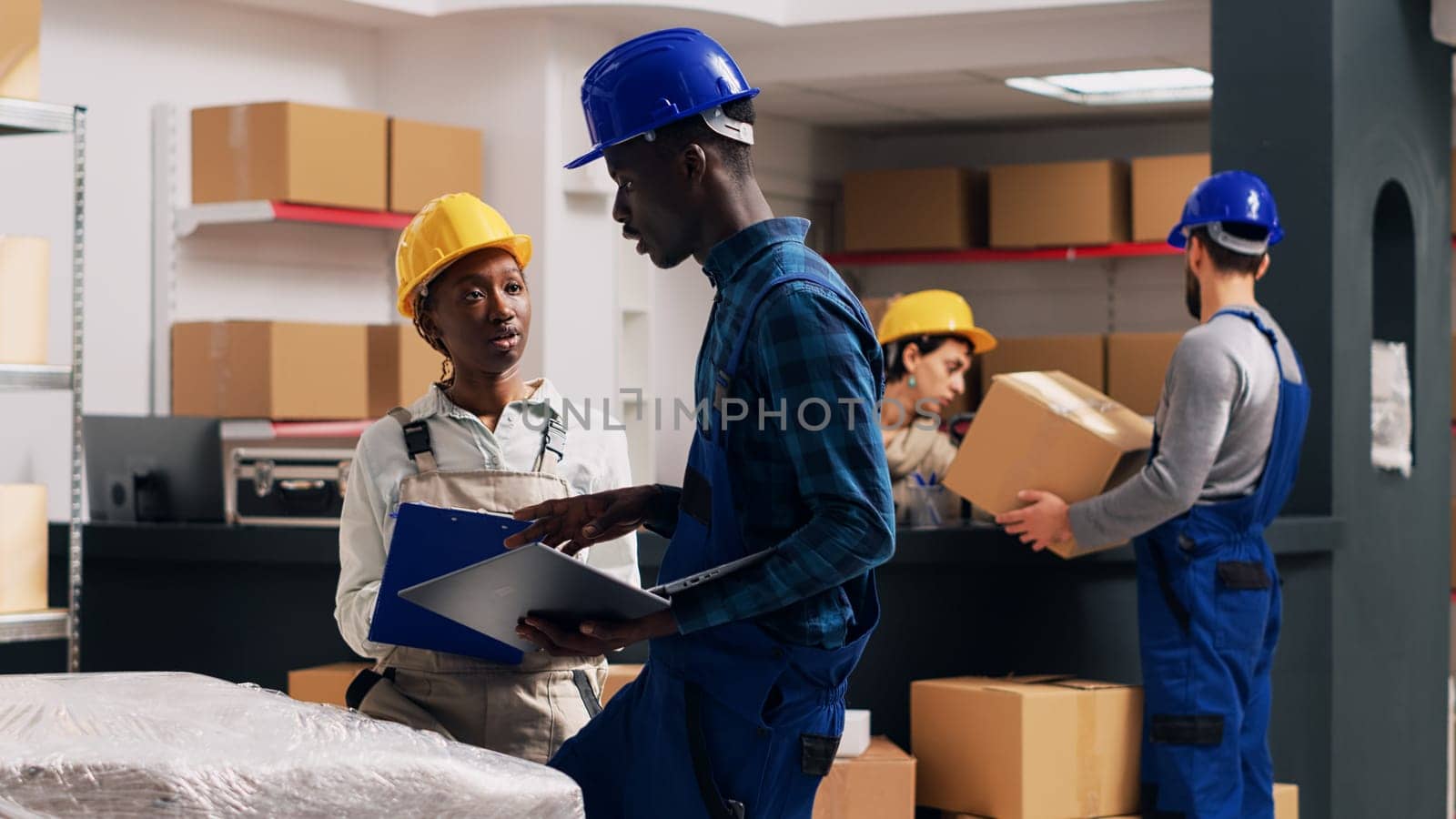 African american people doing quality control in warehouse, working with merchandise from depot shelves. Team of man and woman checking products for industrial service. Handheld shot.