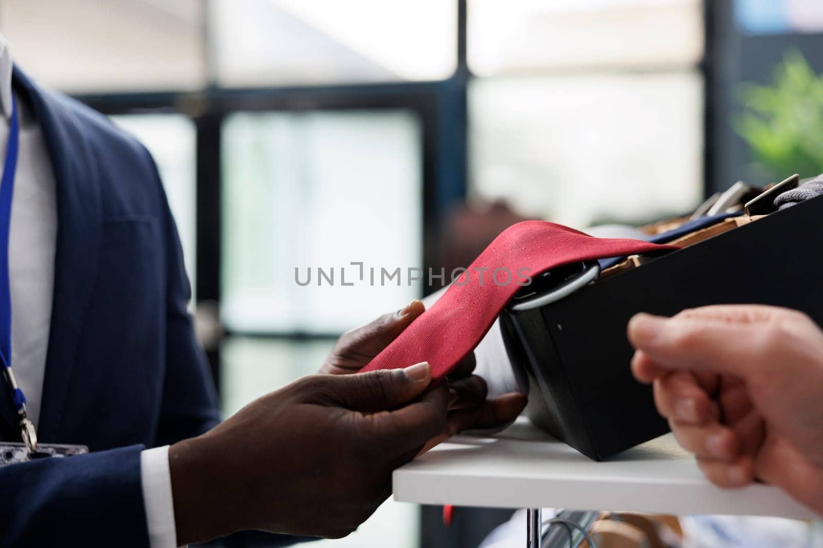 Stylish employee helping elderly shopper with red tie, checking fabric in shopping centre. Senior client buying trendy clothes and fashionable accessories for casual wear in modern boutique. Close up