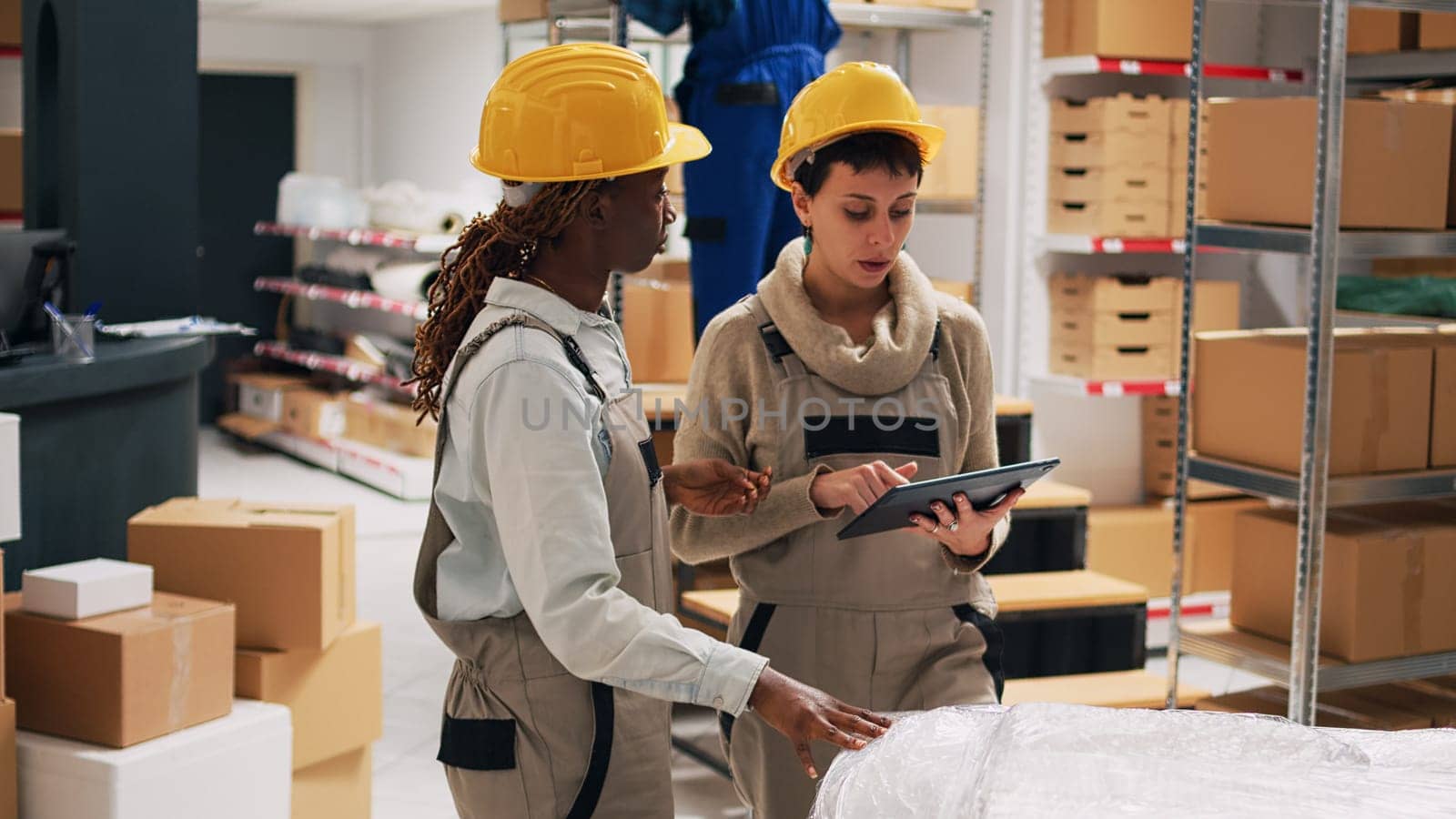 Supervisor and employee using digital tablet to check order logistics in storage room, looking at products packed in boxes on shelves. Team of women planning order shipment in depot.