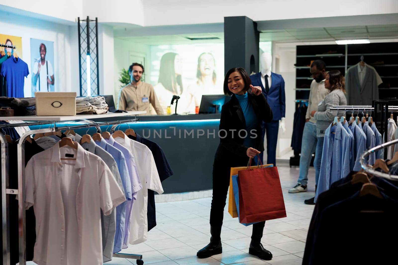 Happy woman shopaholic dancing with shopping bags after making successful purchase in clothing store. Cheerful customer holding paper packages with apparel and moving body to music in mall