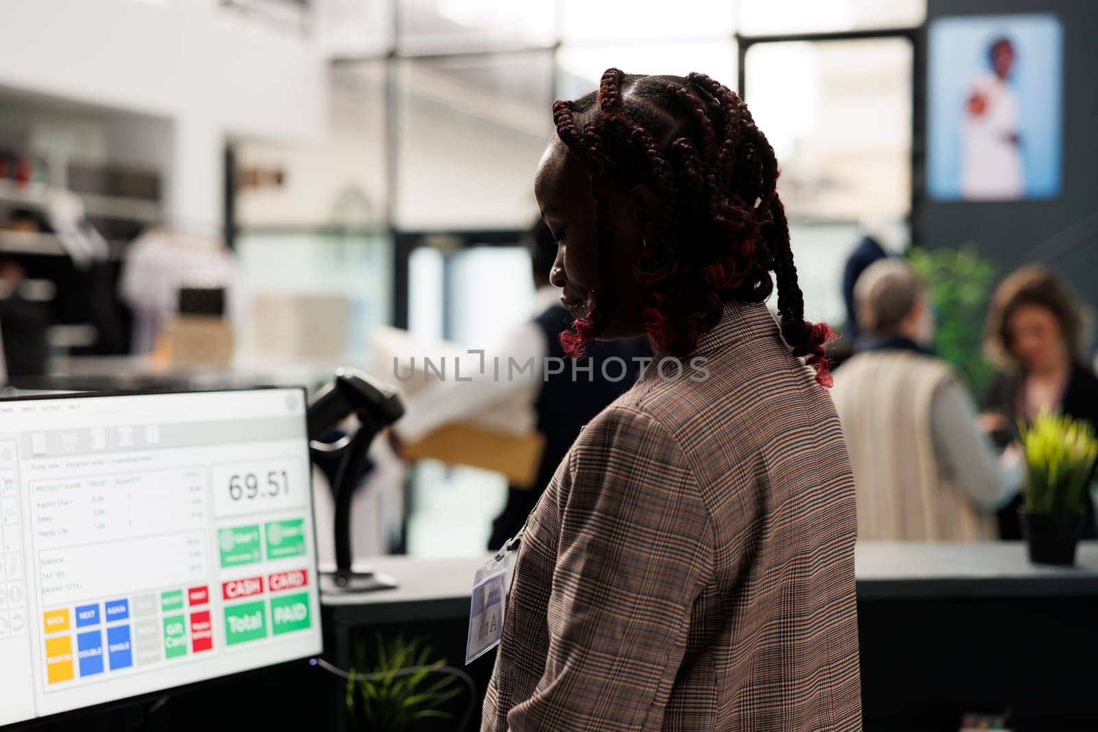 Showroom employee analyzing merchandise inventory on computer, working at clients purchase report in shopping centre. African american worker standing at cash register in modern boutique