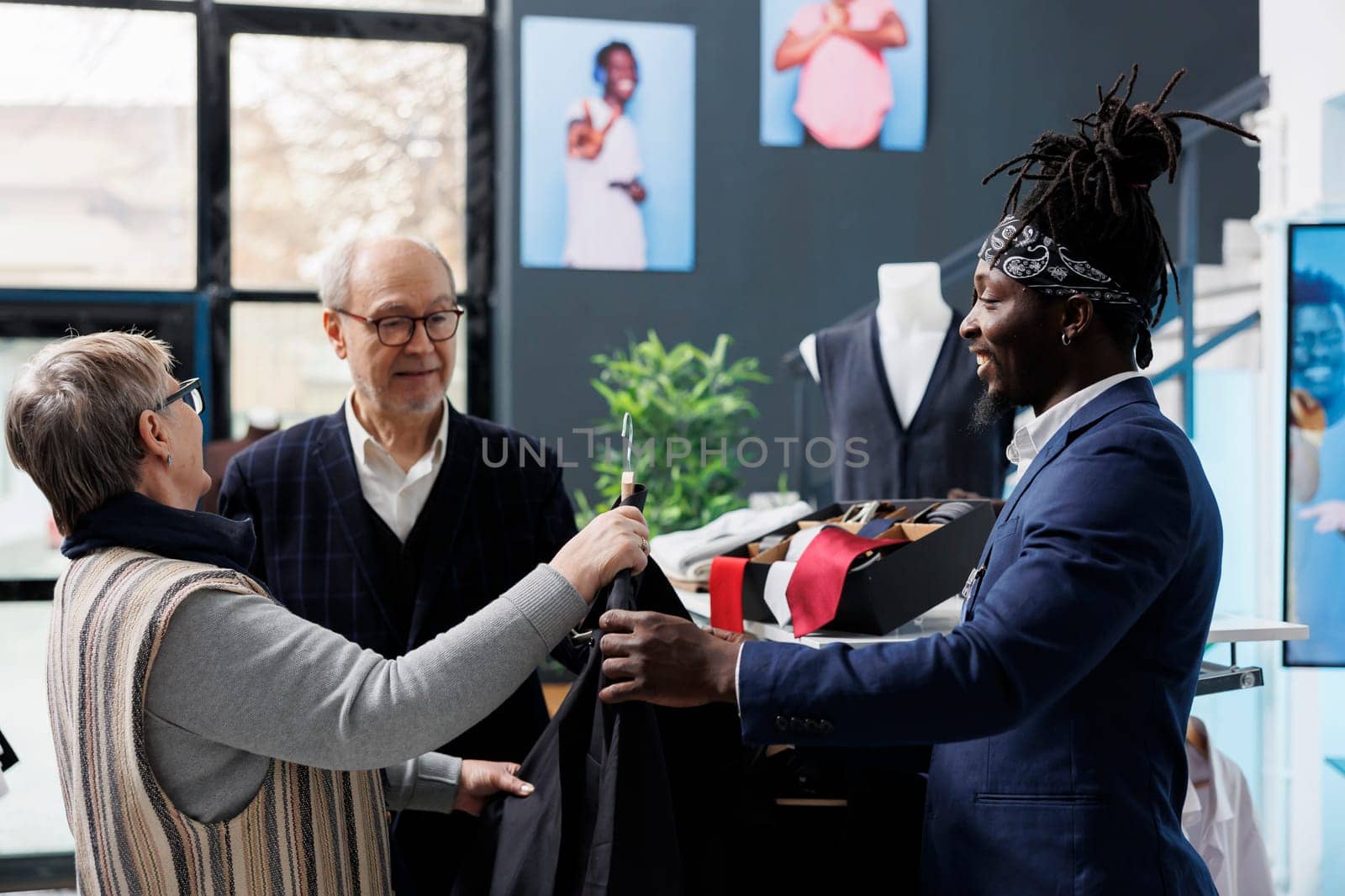 Old couple checking shirt material with boutique employee, buying trendy clothes for casual wear in clothing centre. Elderly customer looking at fashion collection in shopping centre. Fashion concept
