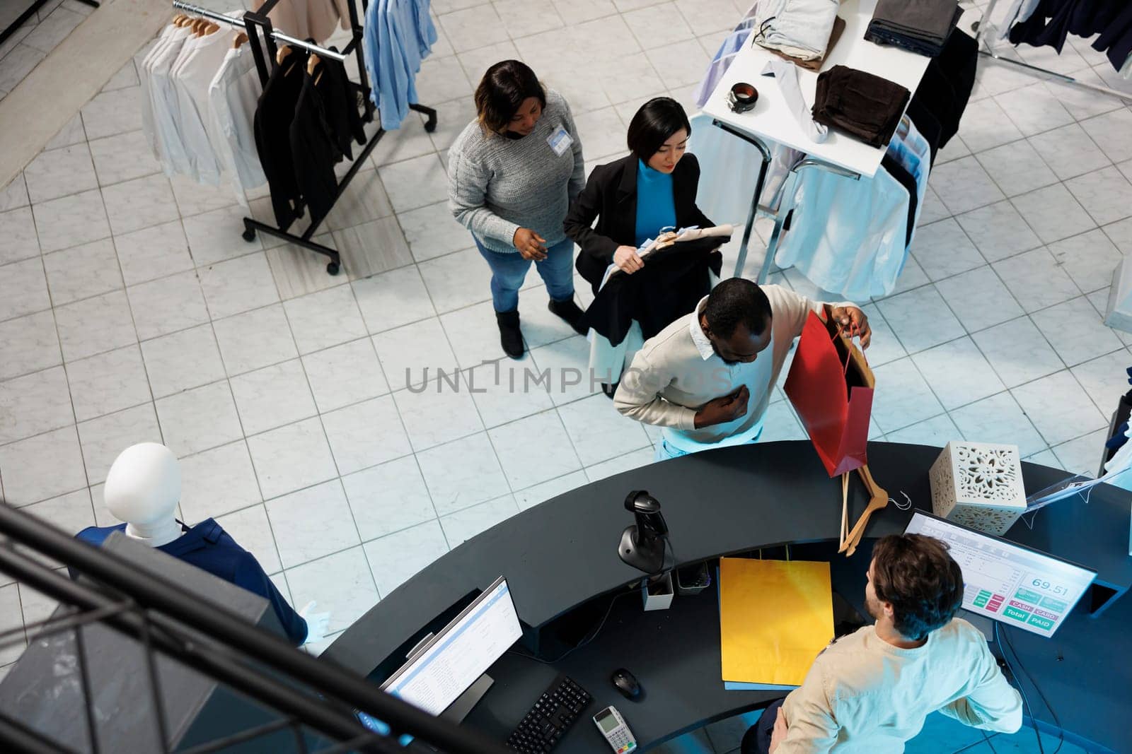 Diverse people waiting in line to pay for selected clothes at department mall checkout desk top view. African american man taking shopping bag from cashier at store cash register