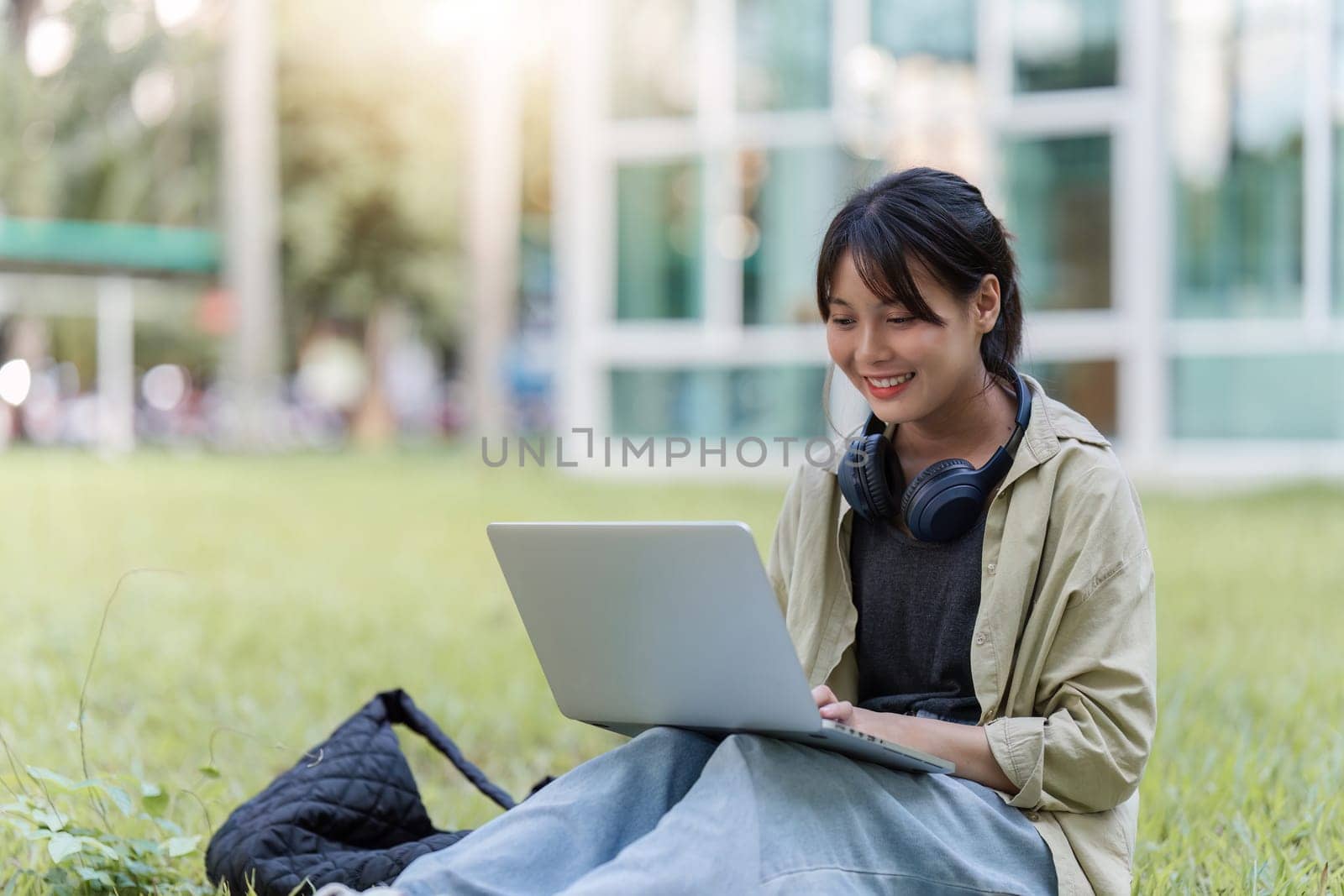 young woman sitting on the grass in the park working, studying on a laptop by itchaznong