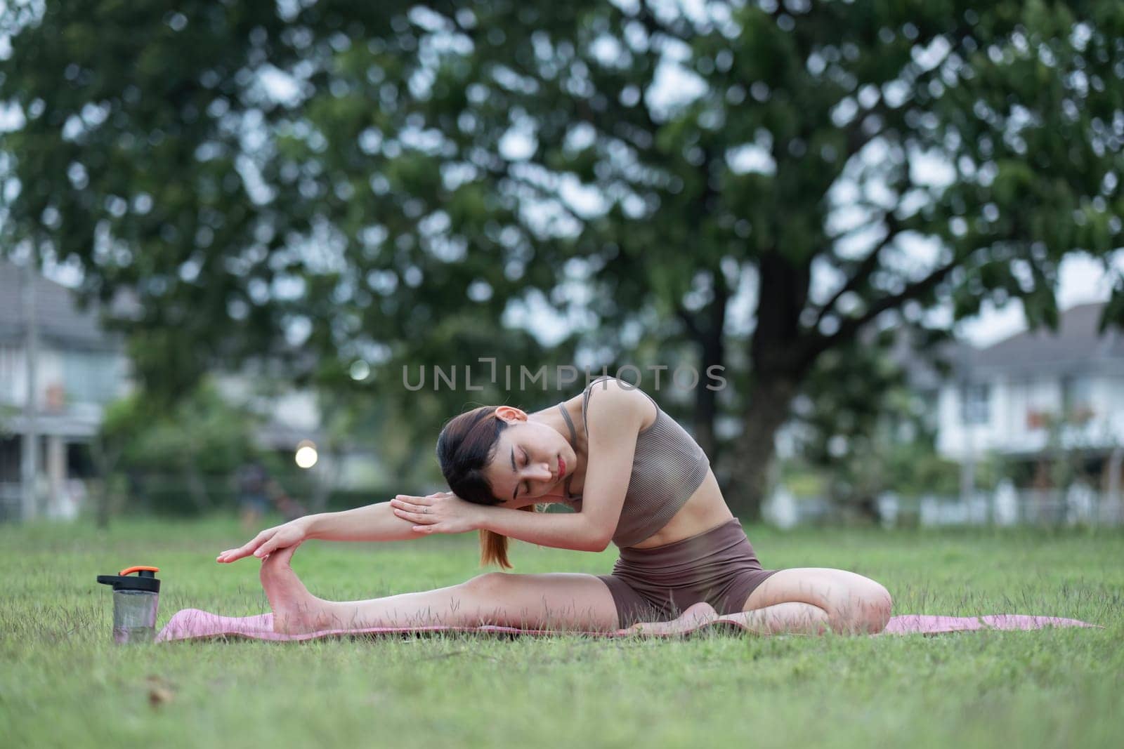 Young healthy Asian woman stretch her body on a yoga mat. Do yoga in a lush park Yoga and Pilates concept by wichayada