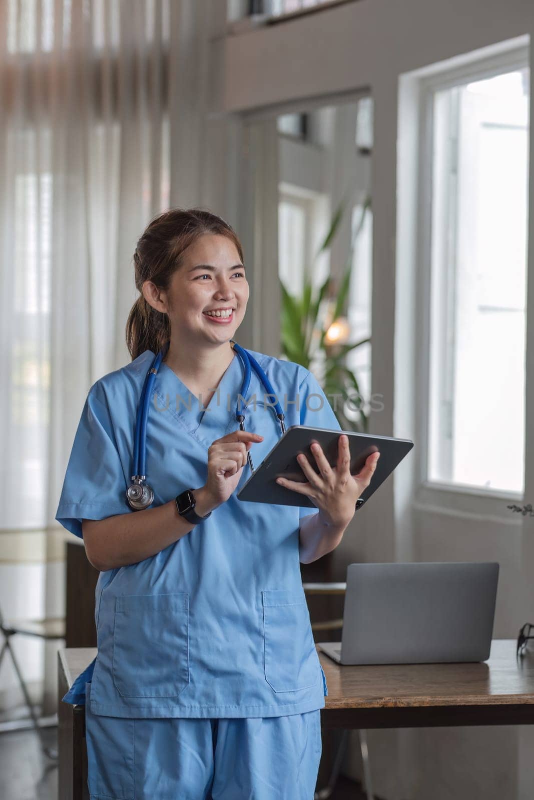 Portrait of a smiling female doctor holding a digital tablet wearing a medical coat and stethoscope in hospital by wichayada