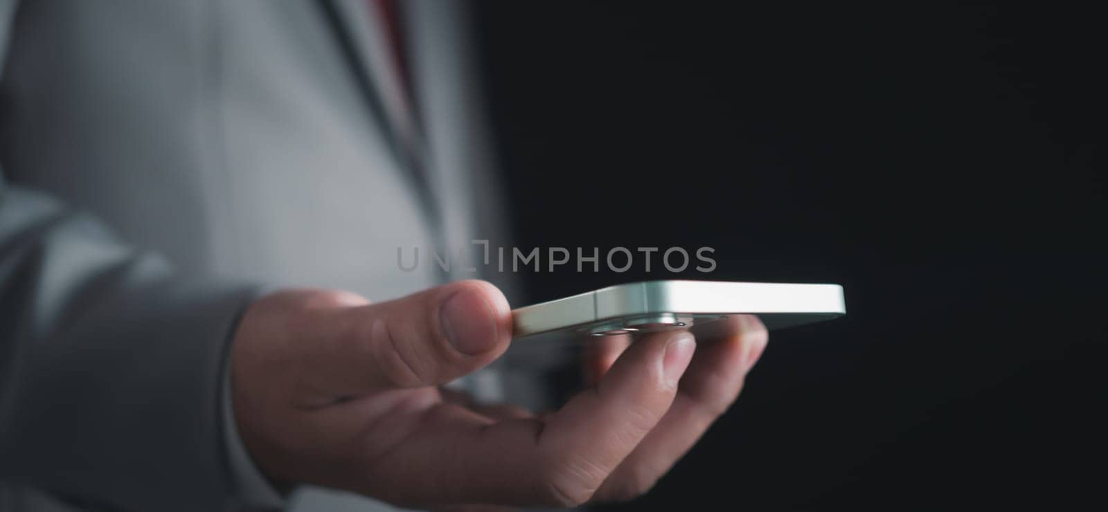 Close-up shot of businessman holding smartphone on dark background Represents business communication concepts.