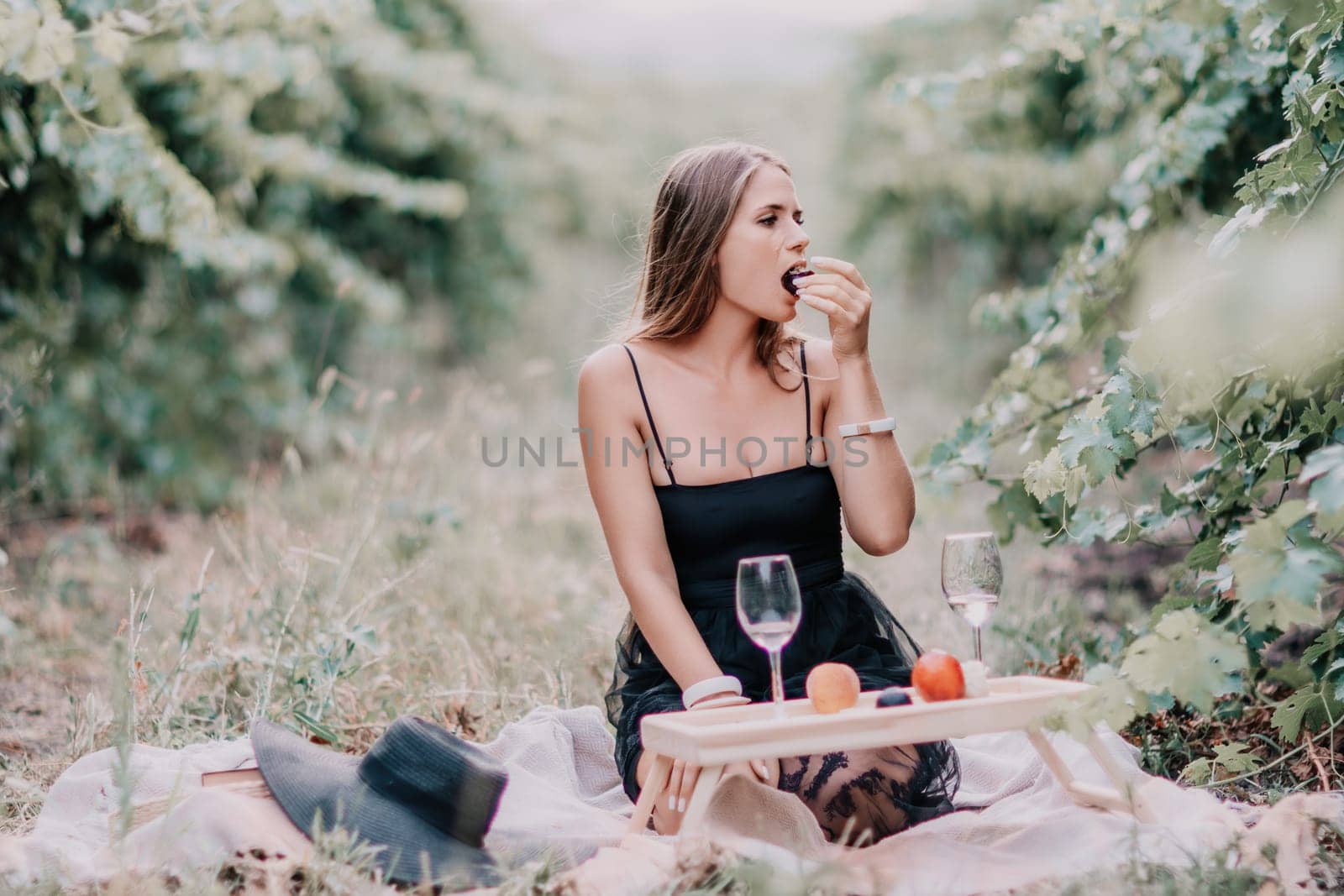 Woman picnic vineyard. Happy woman with a glass of wine at a picnic in the vineyard, wine tasting at sunset and open nature in the summer. Romantic dinner, fruit and wine. by panophotograph