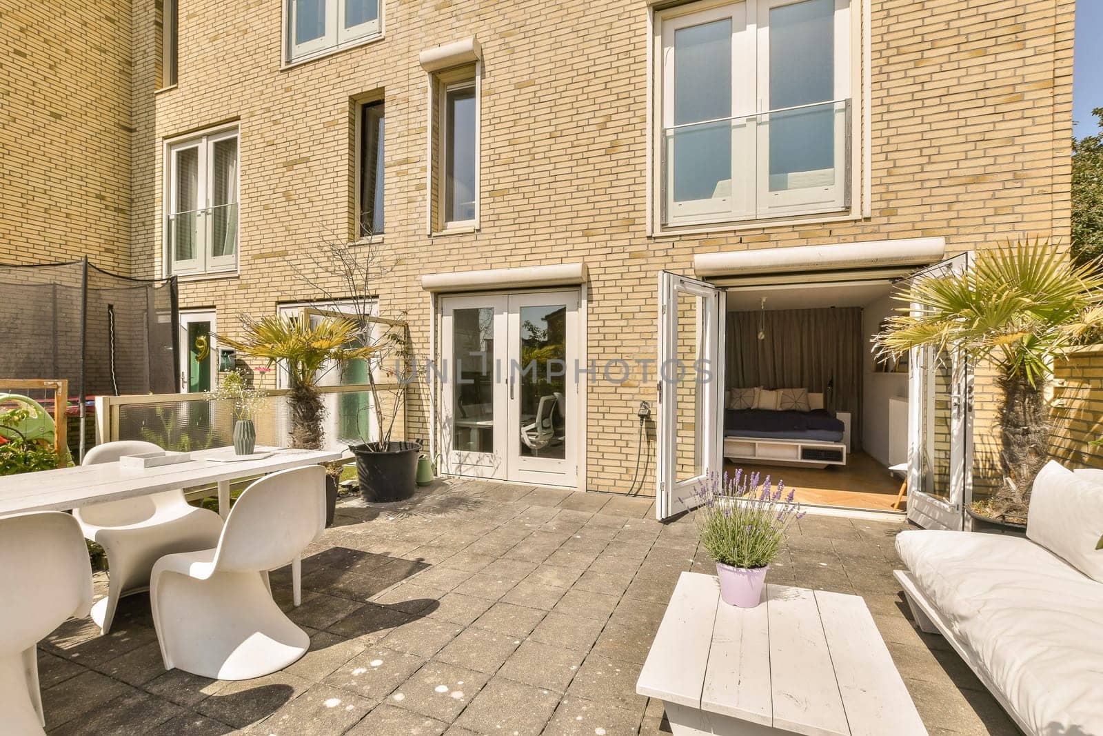 a patio with white furniture and plants on the ground in front of a brick building that is being used as an apartment