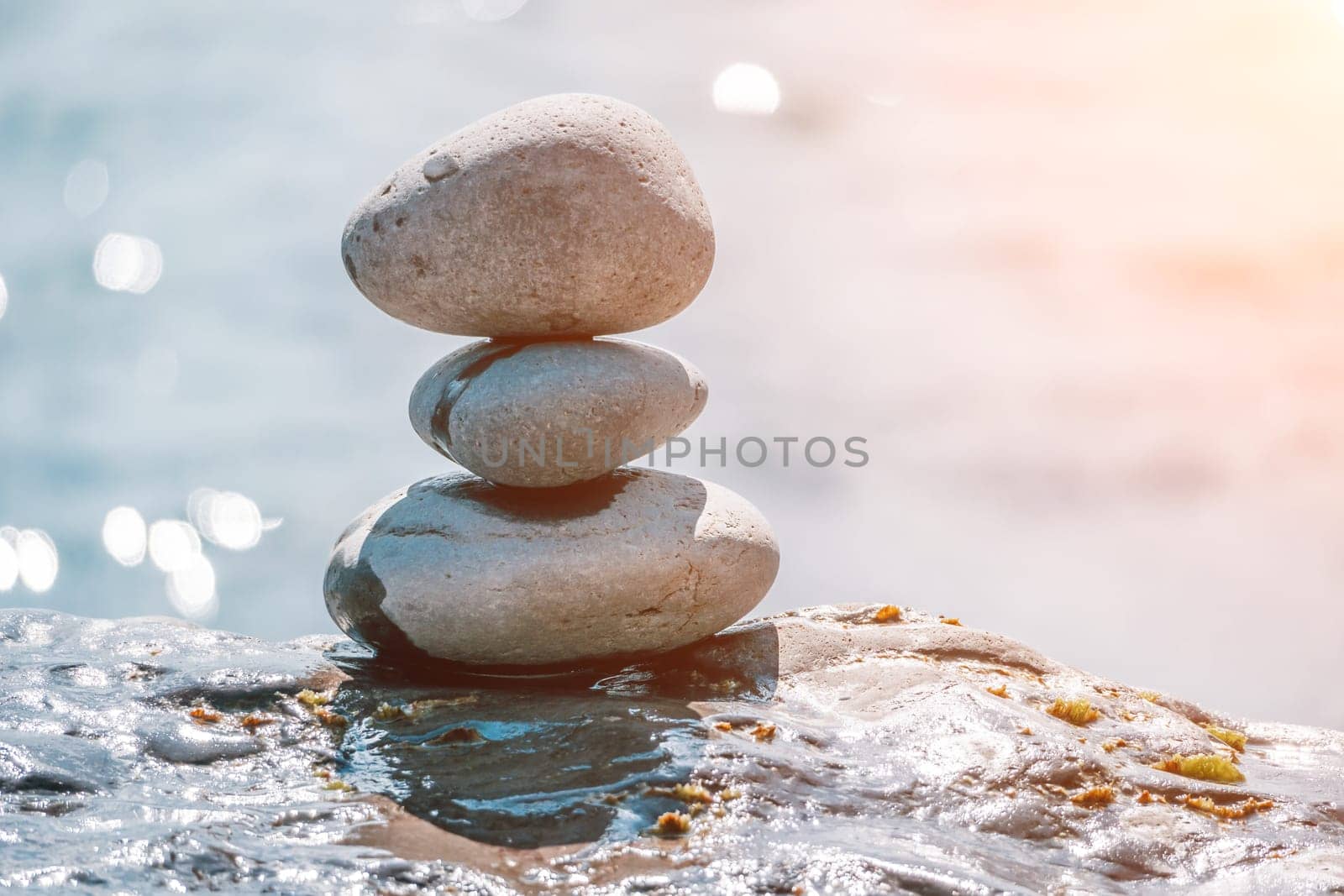 Balanced Pebbles Pyramid on the Beach on Sunny Day and Clear Sky at Sunset. Blue Sea on Background Selective focus, zen stones on sea beach, meditation, spa, harmony, calm, balance concept.