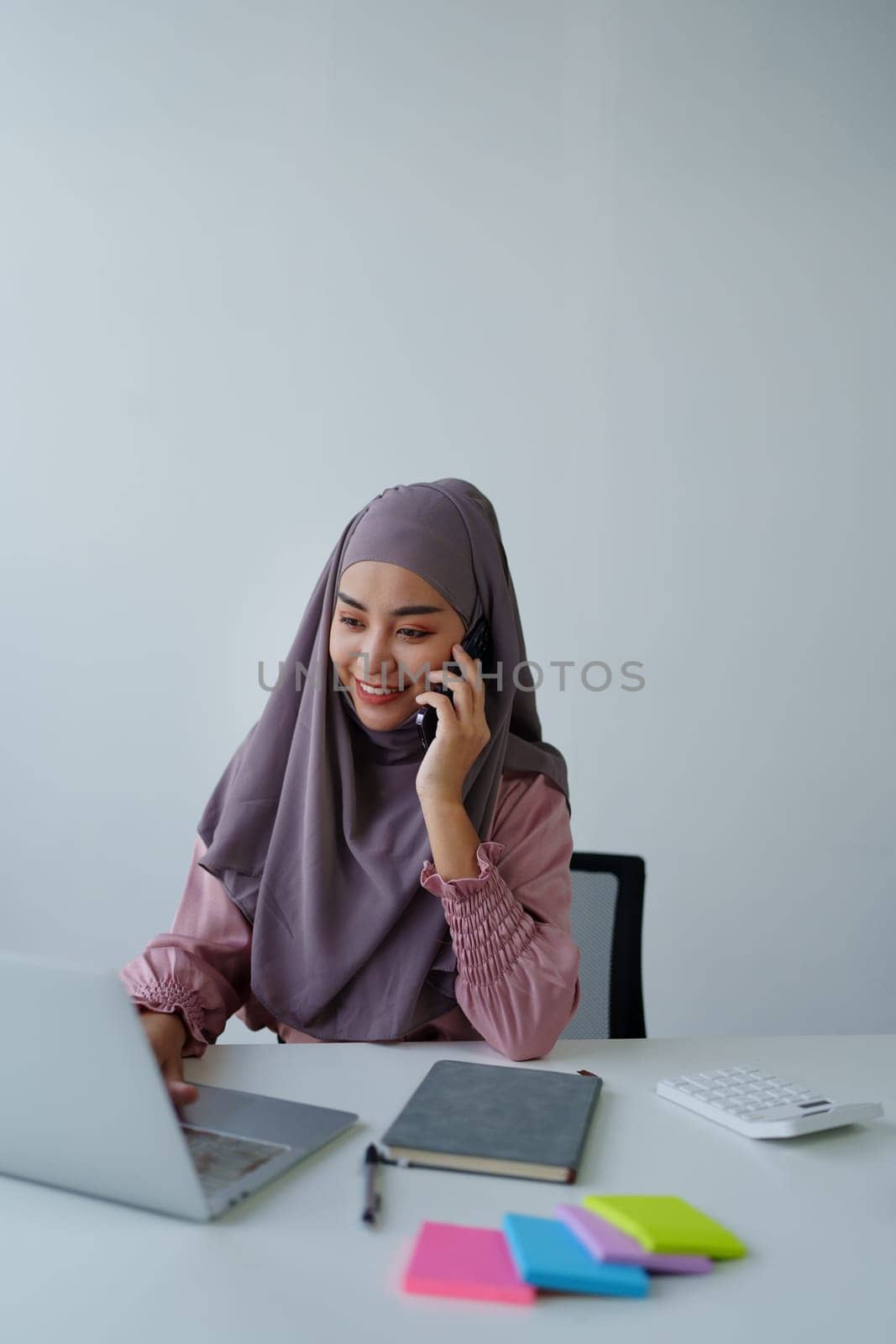 Muslim female employee Using the phone to talk to customers in the office. by Manastrong