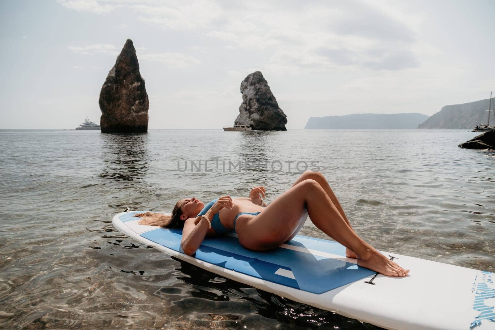 Woman sea sup. Close up portrait of happy young caucasian woman with long hair looking at camera and smiling. Cute woman portrait in bikini posing on sup board in the sea by panophotograph