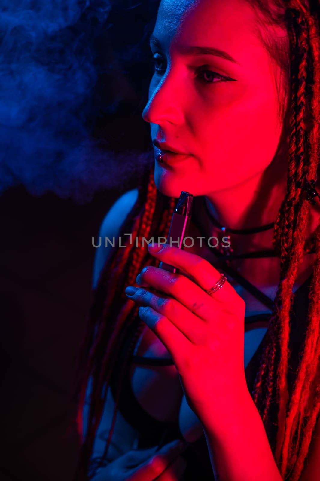 Caucasian girl with dreadlocks smokes a vape in red blue light