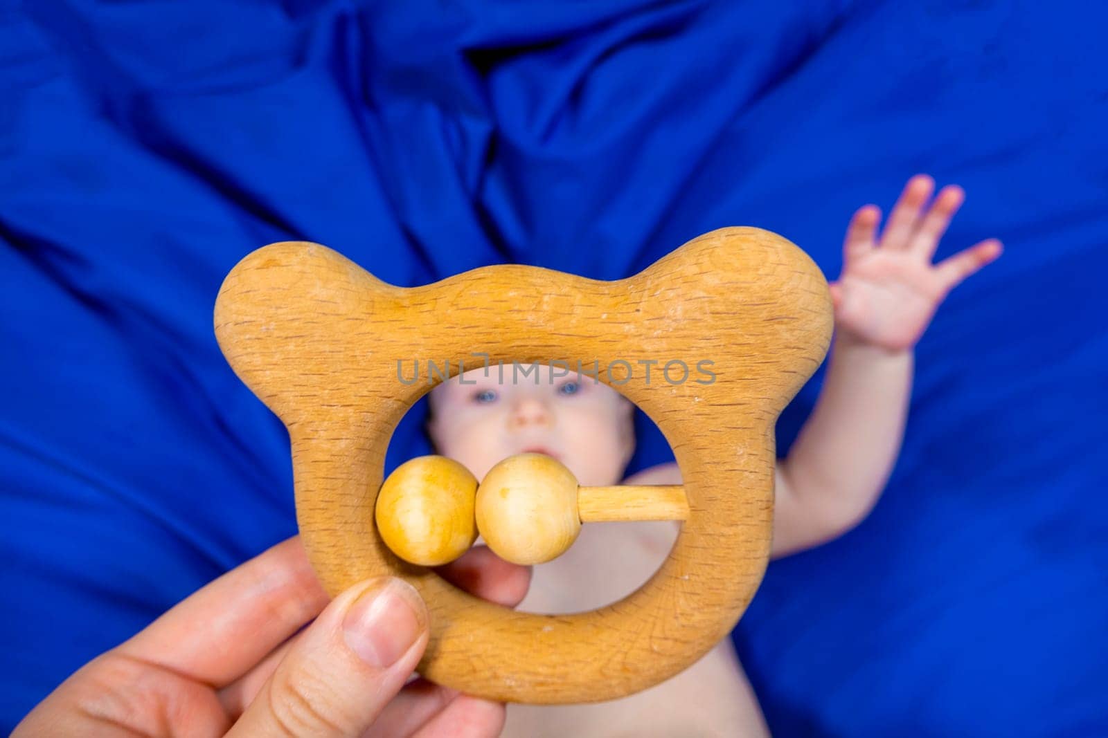 a baby on a blue background with a wooden rattle by kajasja