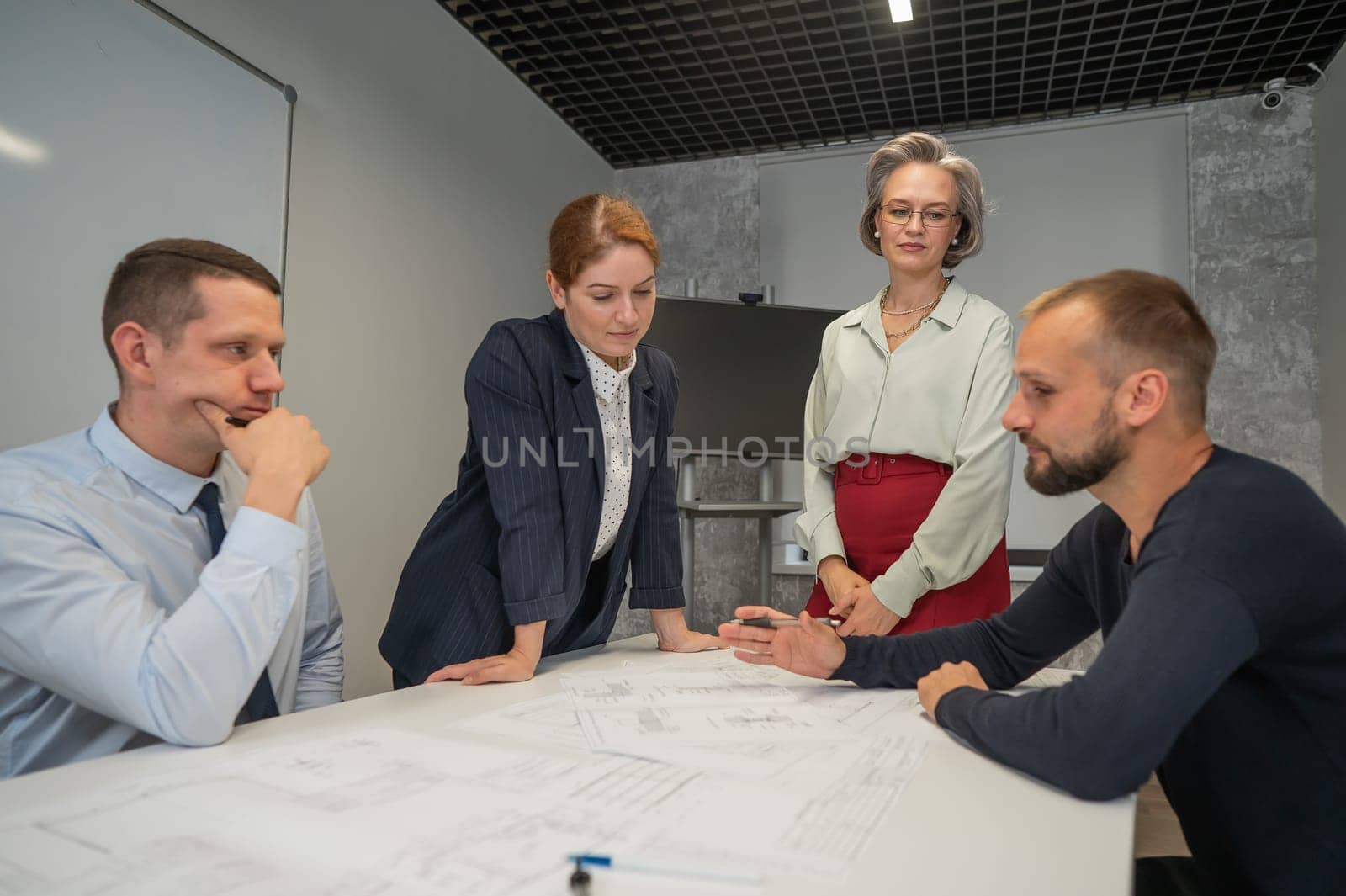 Four business people sitting around a table discussing blueprints. Designers engineers at a meeting