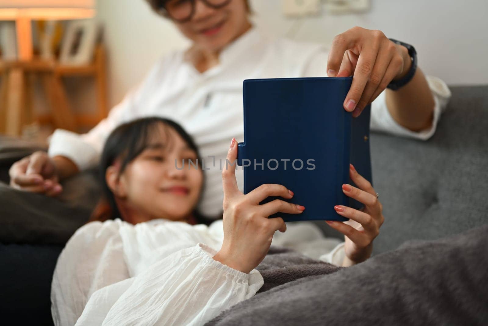 Young couple relaxing on comfortable couch and reading book spending leisure time together at home.