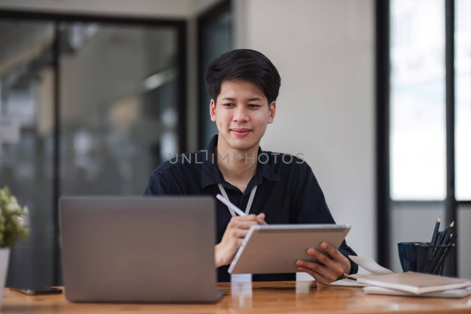 Young businessman uses and tablet to do finance, mathematics on table and wood in office, business, tax, accounting, statistics and analytical research concepts..