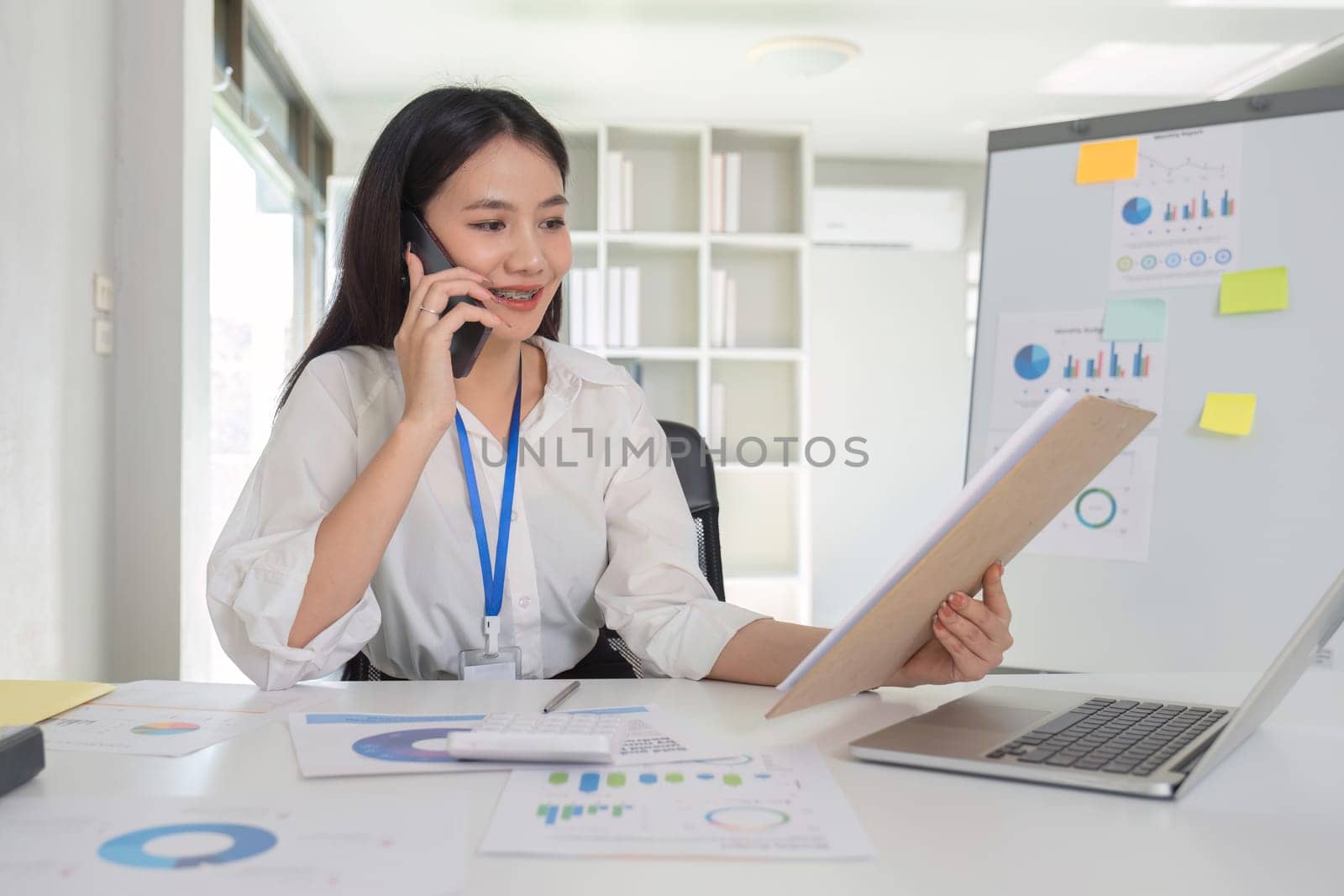 Businesswoman talking on the phone talking with customers and using laptop to do financial management and calculations on white table in office.