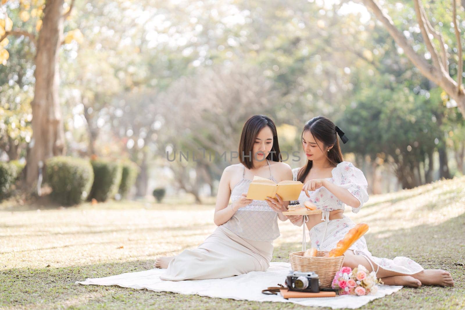 Two beautiful LGBT young women in casual clothes and summer hats Carefree woman having a picnic outside Positive model sitting on the grass eat fruit and cheese Take a selfie. LGBT concept by wichayada