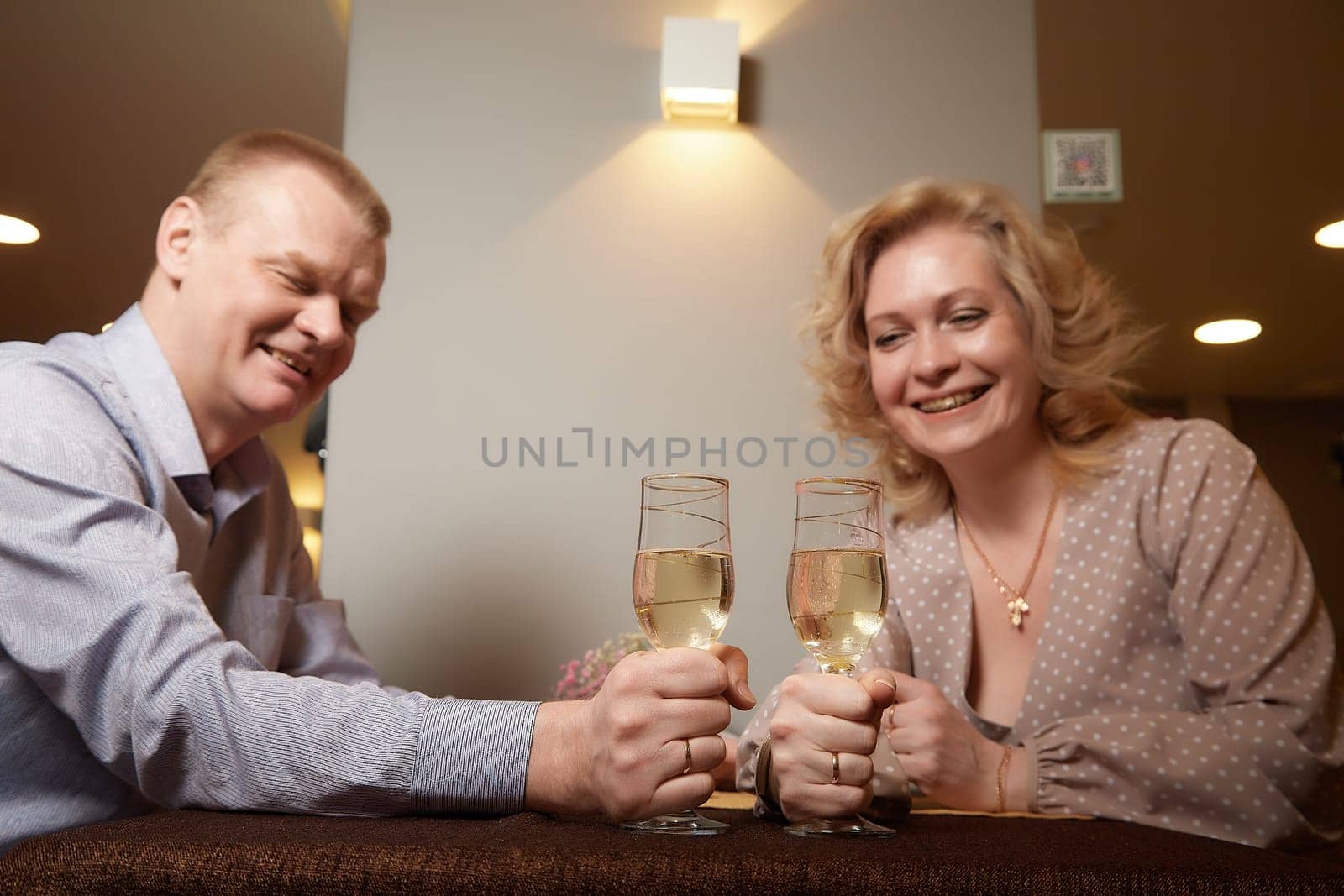 An adult couple drinks wine or champagne in an intimate setting inside of the room or restaurant. A man and a woman on an evening date. Family and love by keleny