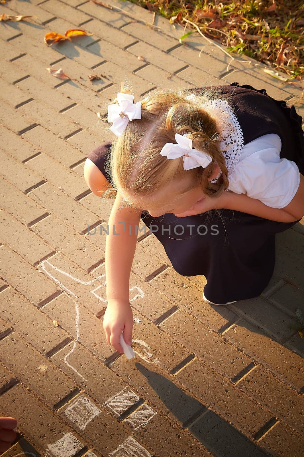 Little girl of elementary school student in modern school uniform drawing with chalk on asphalt outdoors. Female child schoolgirl going to school. Back to school in september 1
