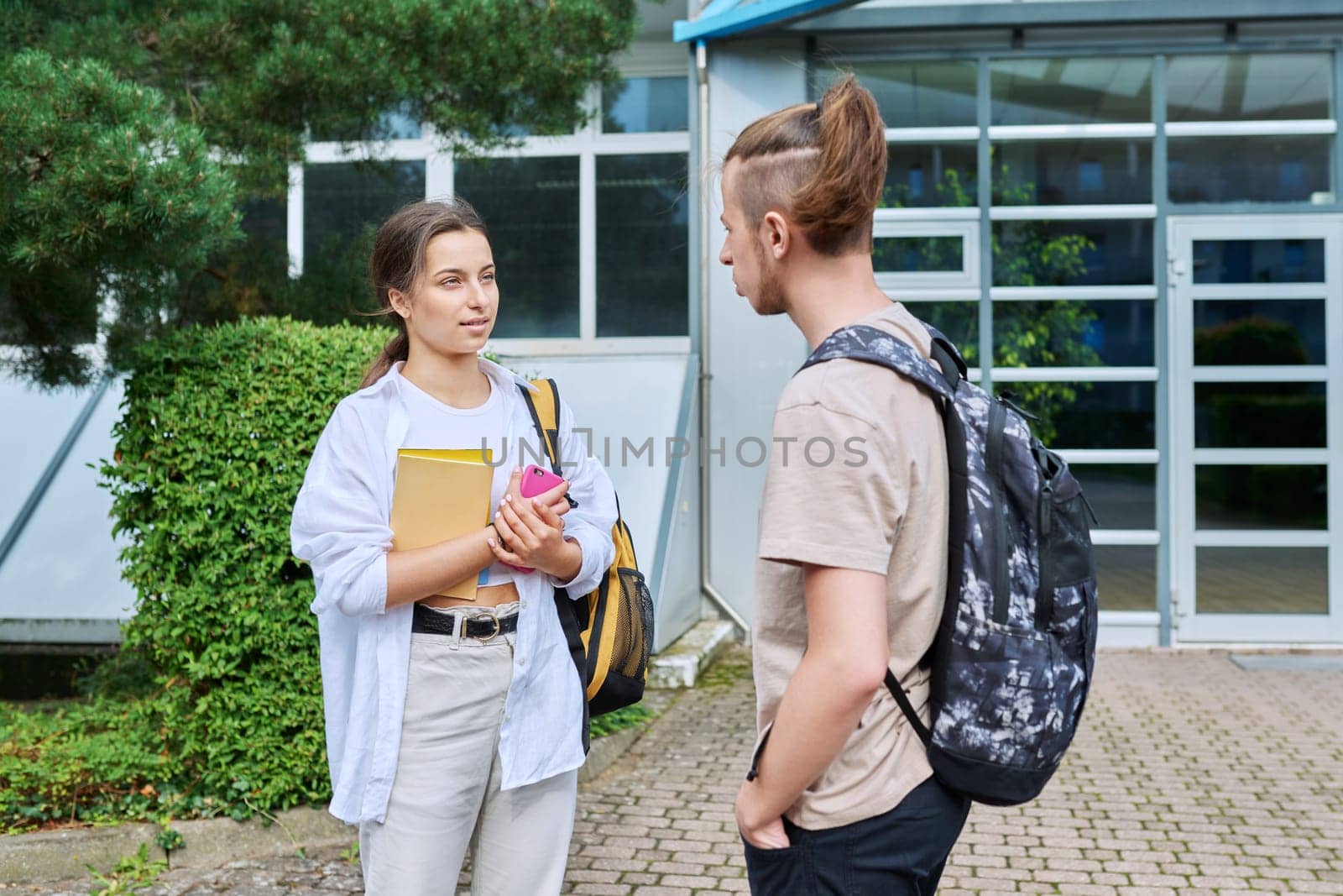 Meeting of two teenage students, guy and girl, outdoors near educational building. Friendship, communication, education, high school college concept