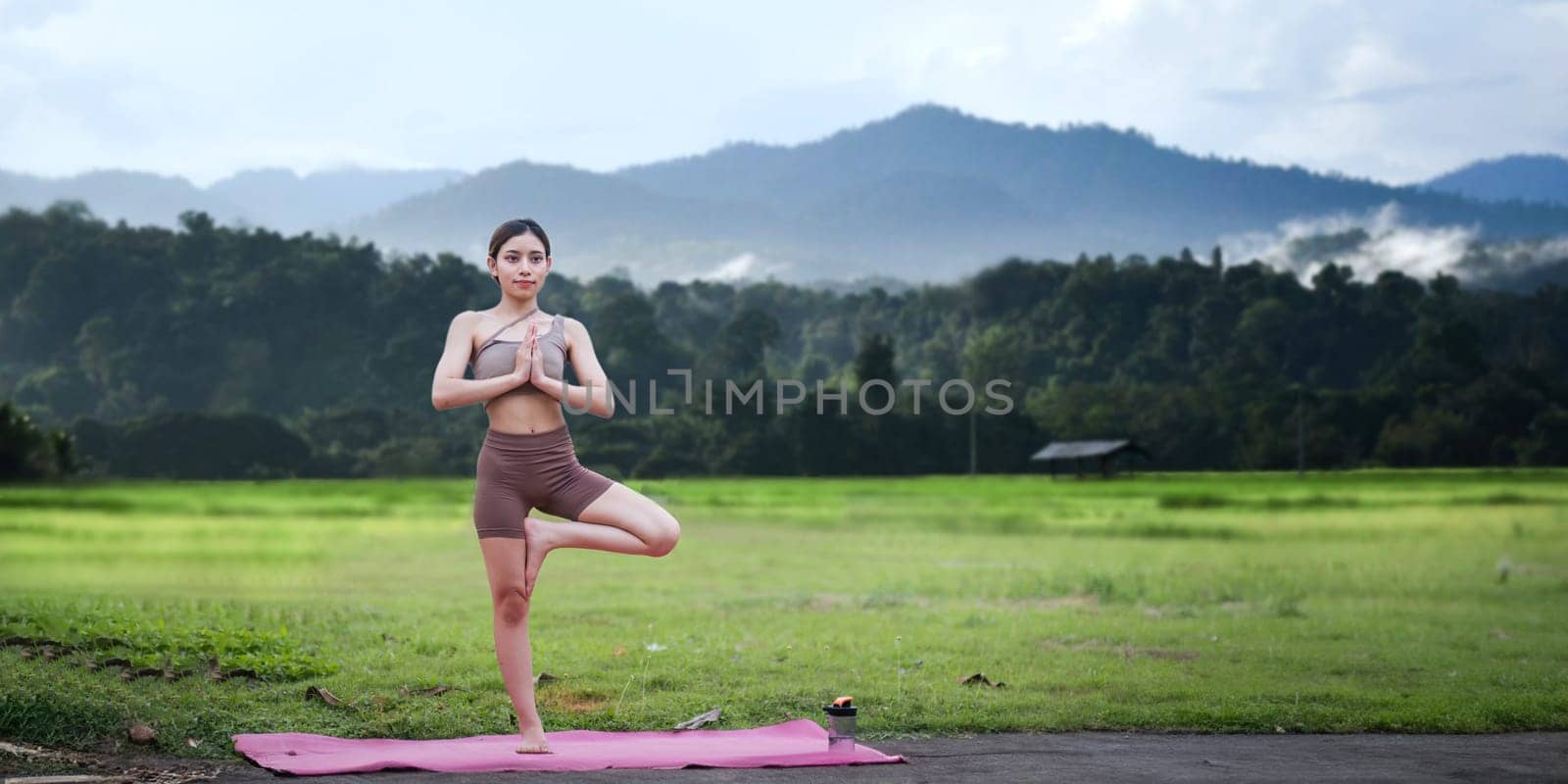 Asian woman standing on fitness mat, sporty lady practicing yoga at public park outdoor, stretching her body. Healthy active lifestyle by nateemee