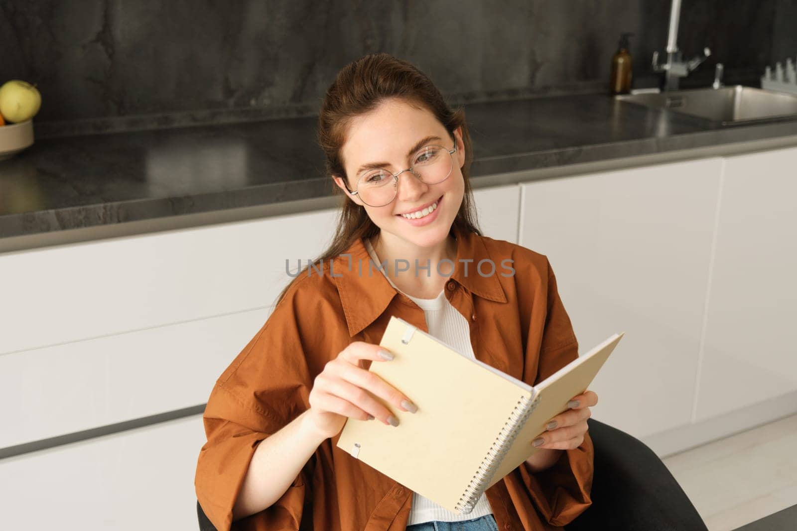 Close up portrait of young woman, student in kitchen, holding notebook, revising for exam at home, studying, reading her planner.