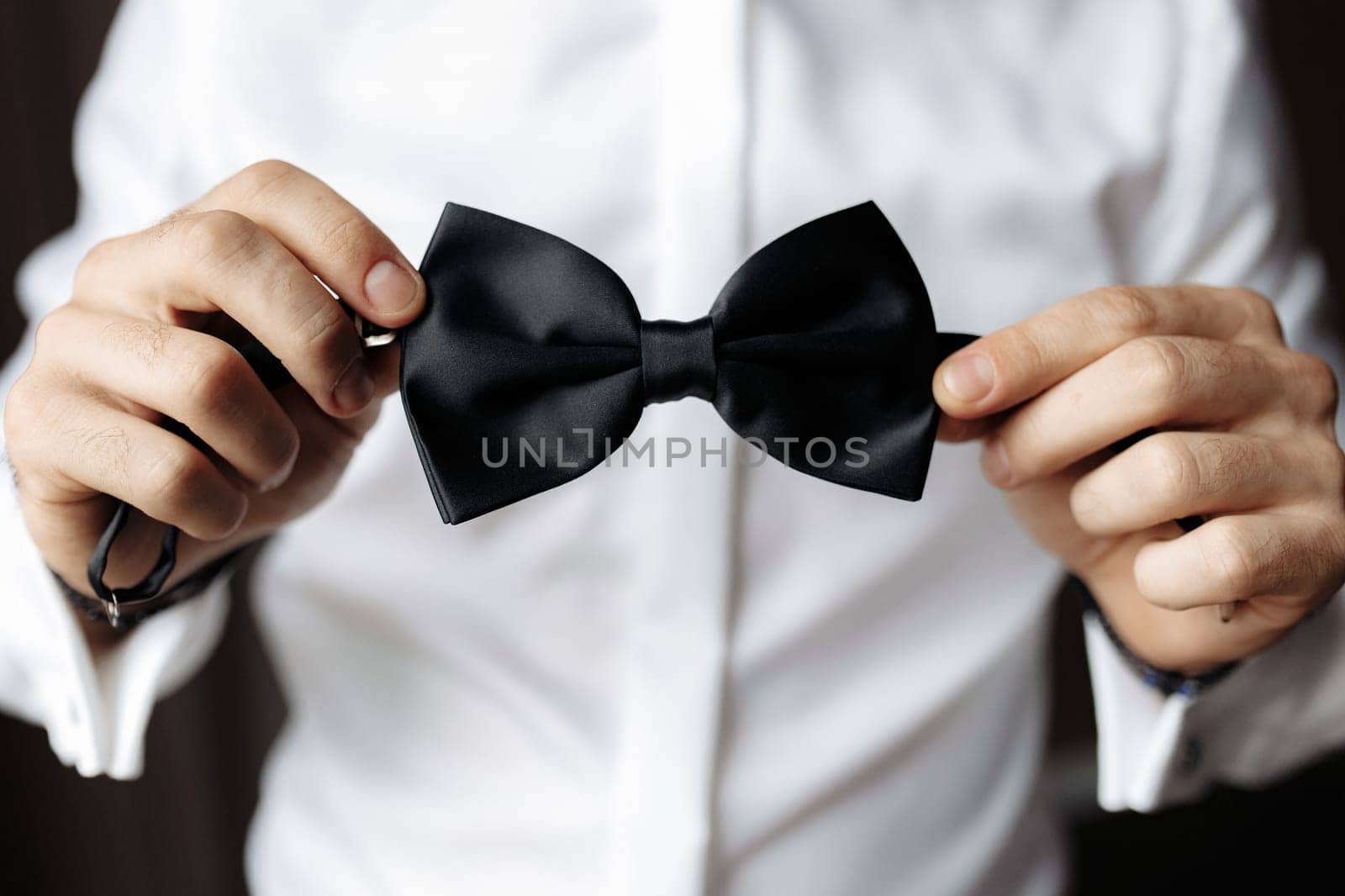 Partial close up view of man holding black bow tie. Soft focus high quality image.