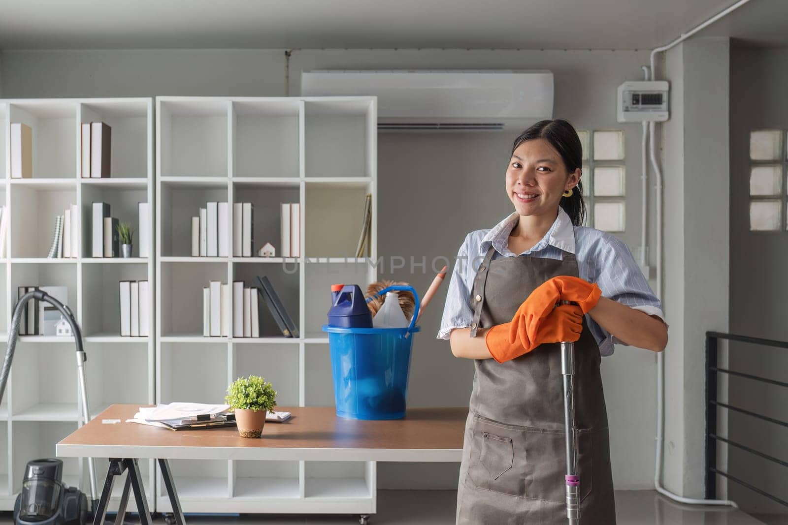 Portrait of a beautiful young housewife smiling and happy, holding cleaning supplies in the office. cleaning supplies, housekeeper.