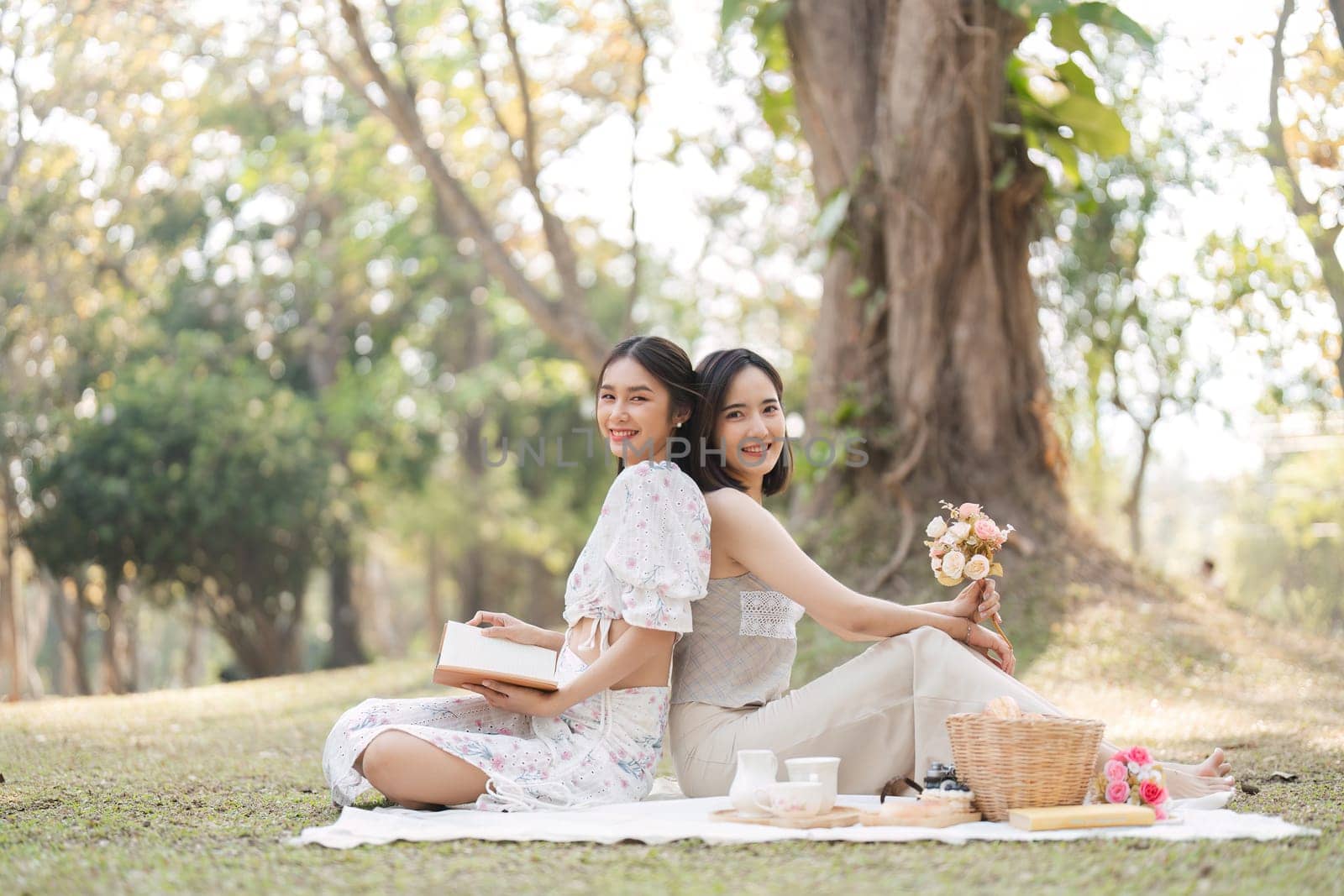 Two beautiful LGBT young women in casual clothes and summer hats Carefree woman having a picnic outside Positive model sitting on the grass eat fruit and cheese Take a selfie. LGBT concept by wichayada